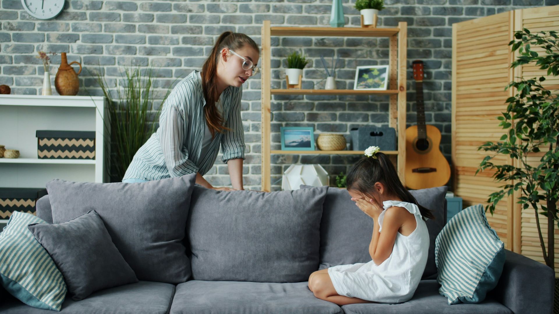 Mother scolds crying daughter on sofa in living room.