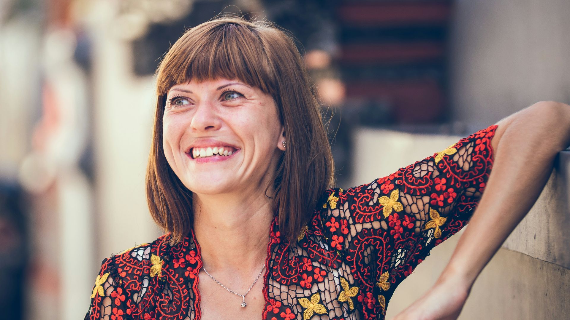 woman in floral-themed cardigan leaning on fence in bokeh photography