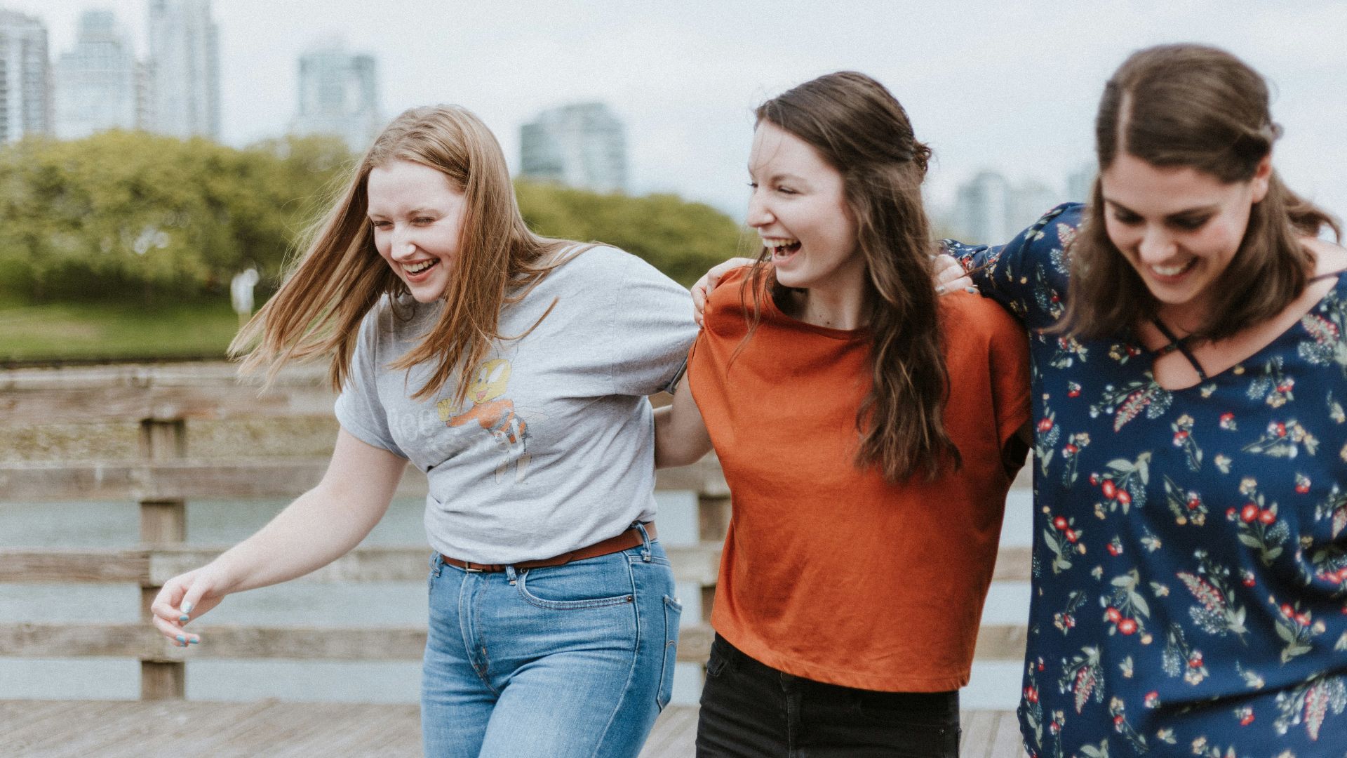 three women walking on brown wooden dock near high rise building during daytime