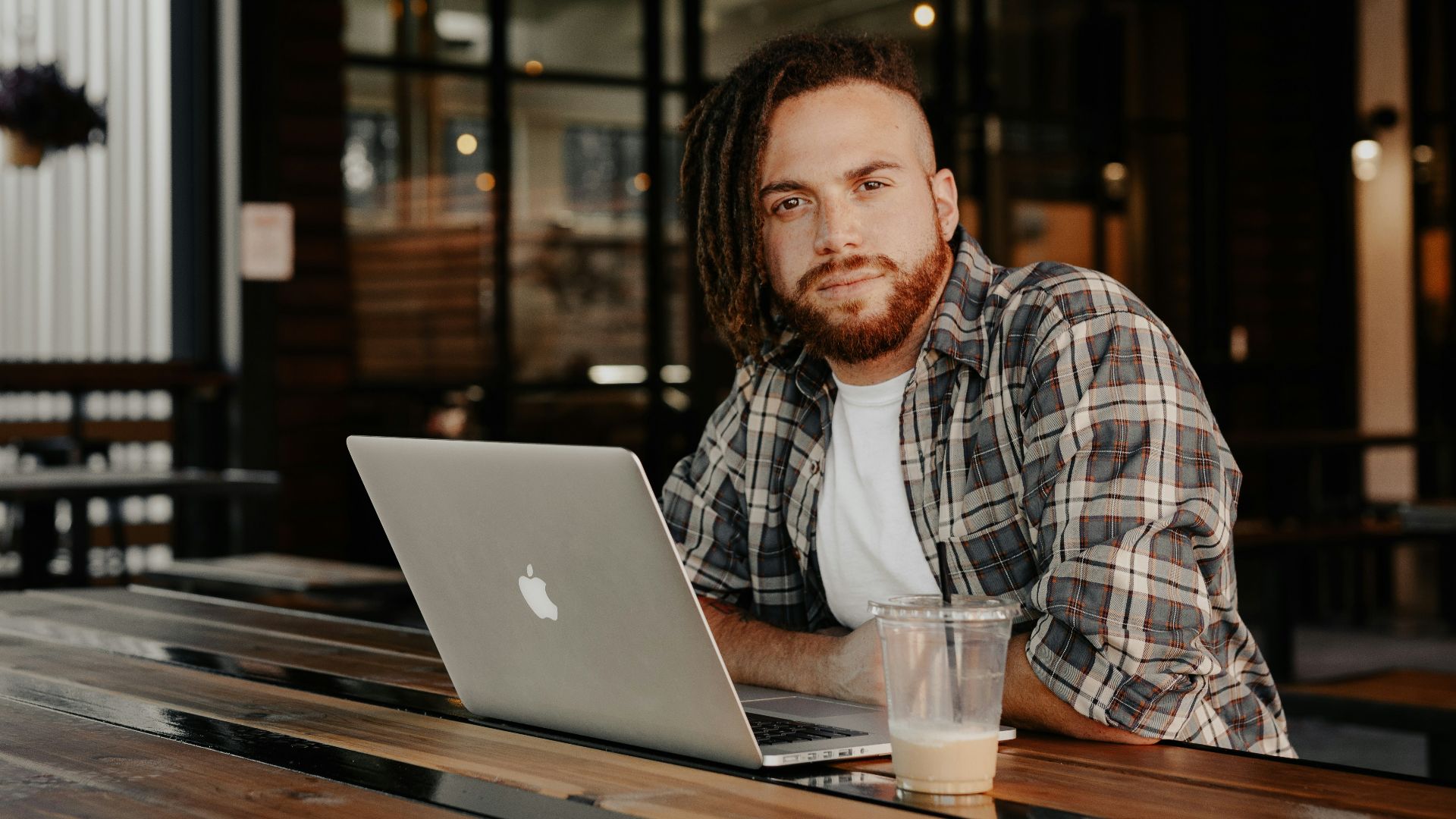 man in black and white plaid dress shirt sitting by the table using macbook