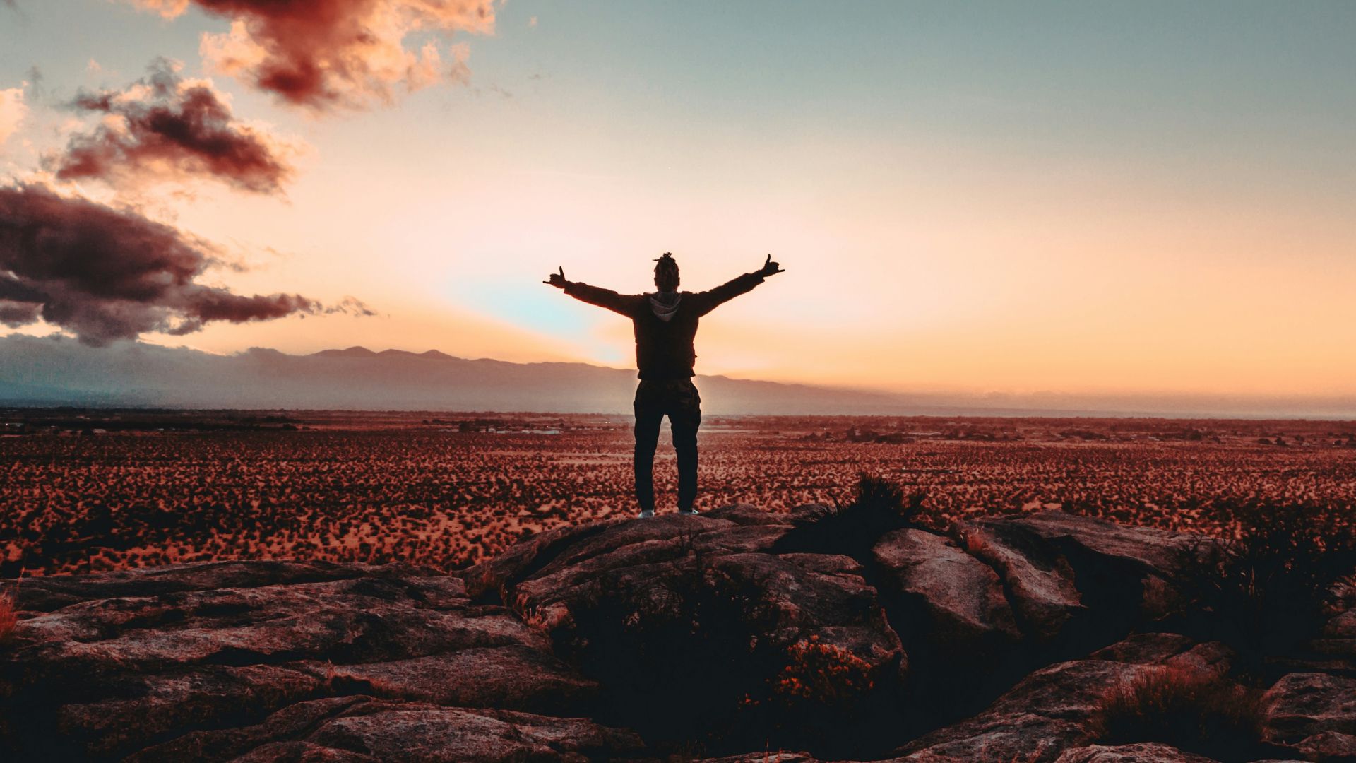 person standing on rock raising both hands
