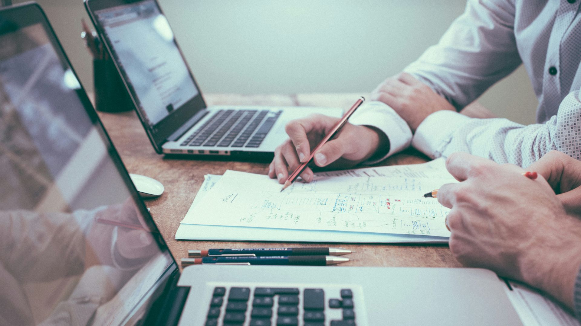 person holding pencil near laptop computer