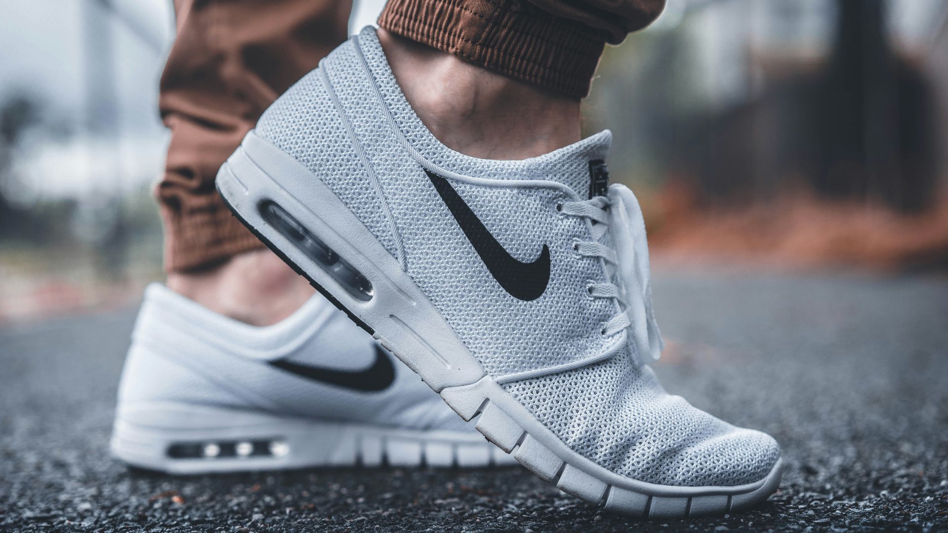 person wearing white Nike running shoes standing on black concrete path