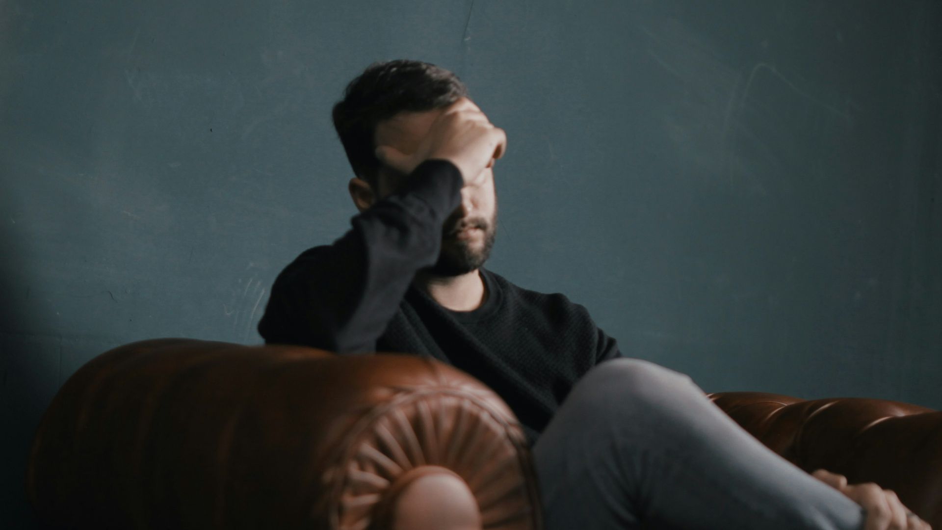 a man holds his head while sitting on a sofa