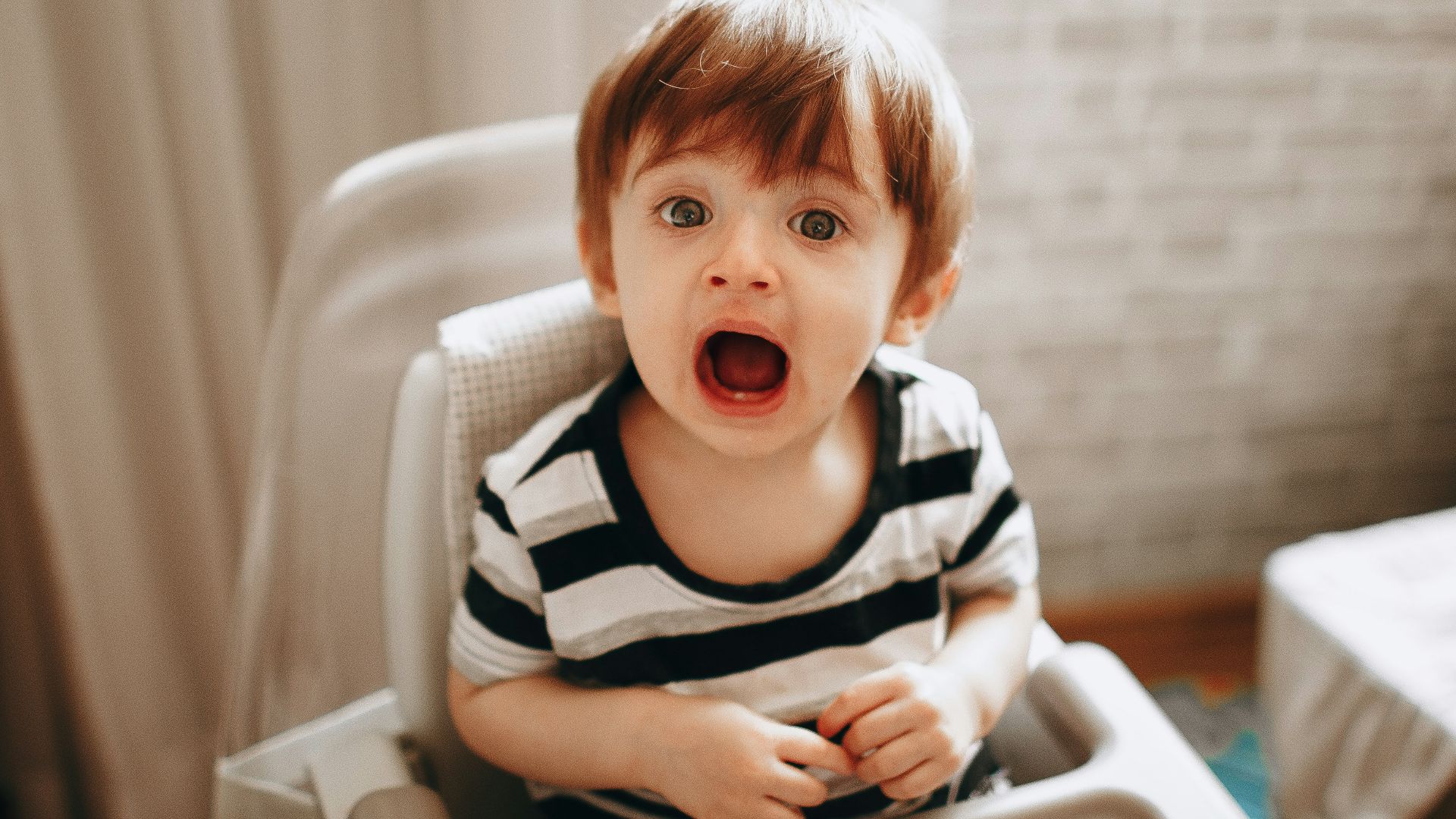 boy in black and white striped shirt sitting on white high chair