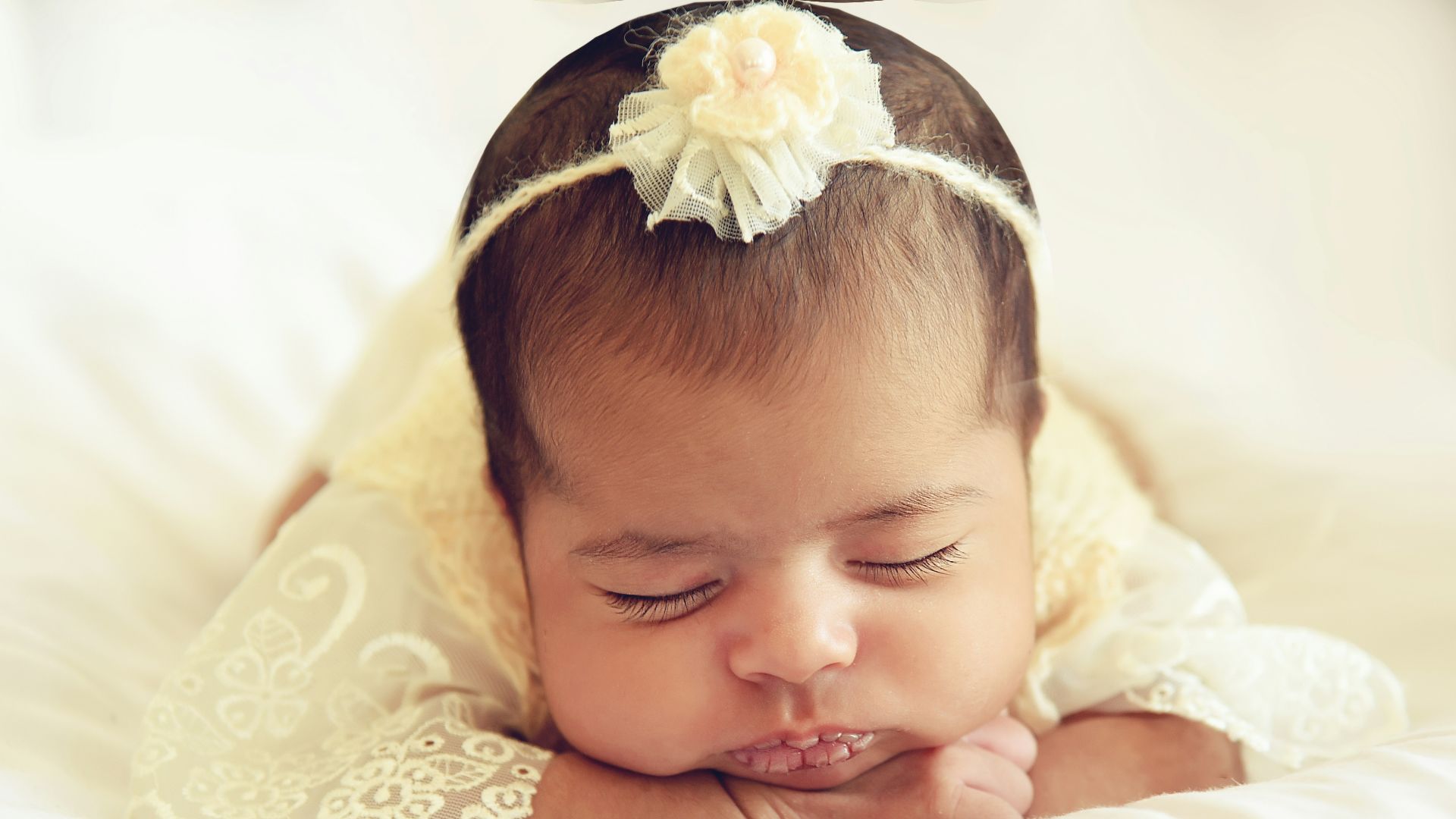 baby in white dress lying on white textile