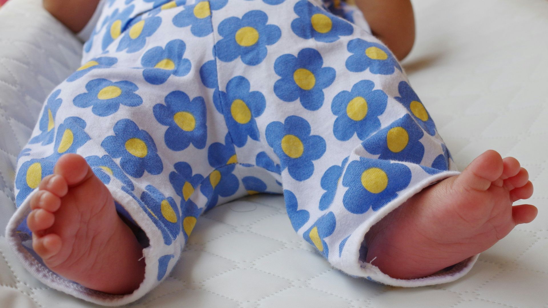 a baby laying on a bed with a blue and yellow flowered outfit
