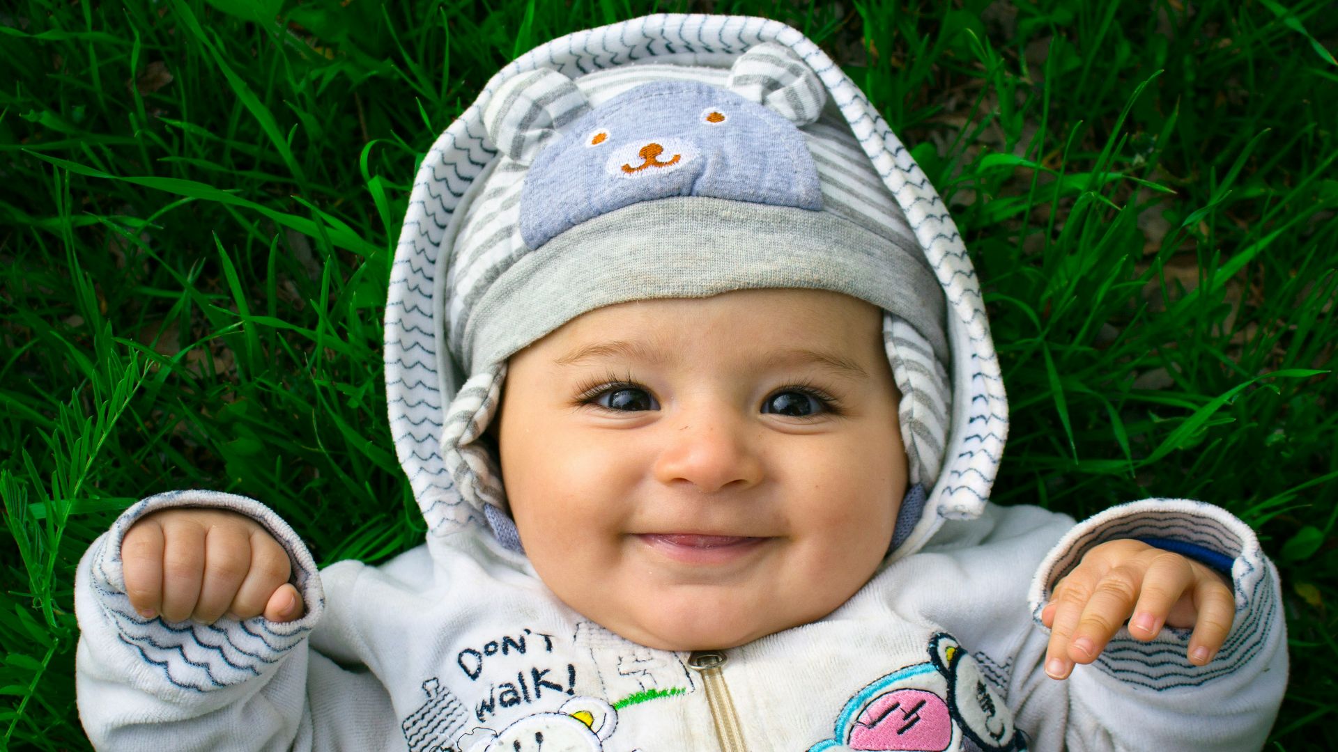 Smiling baby lies on the grass, looking happy.