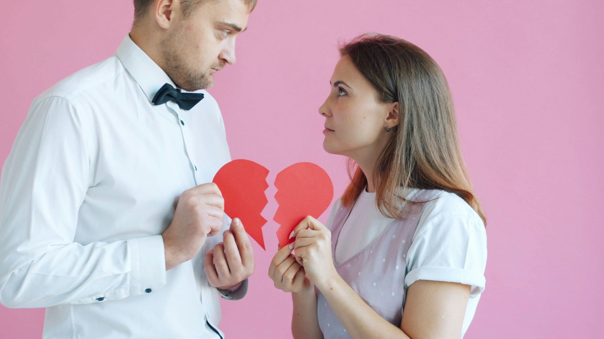 Couple holding broken heart halves on pink background