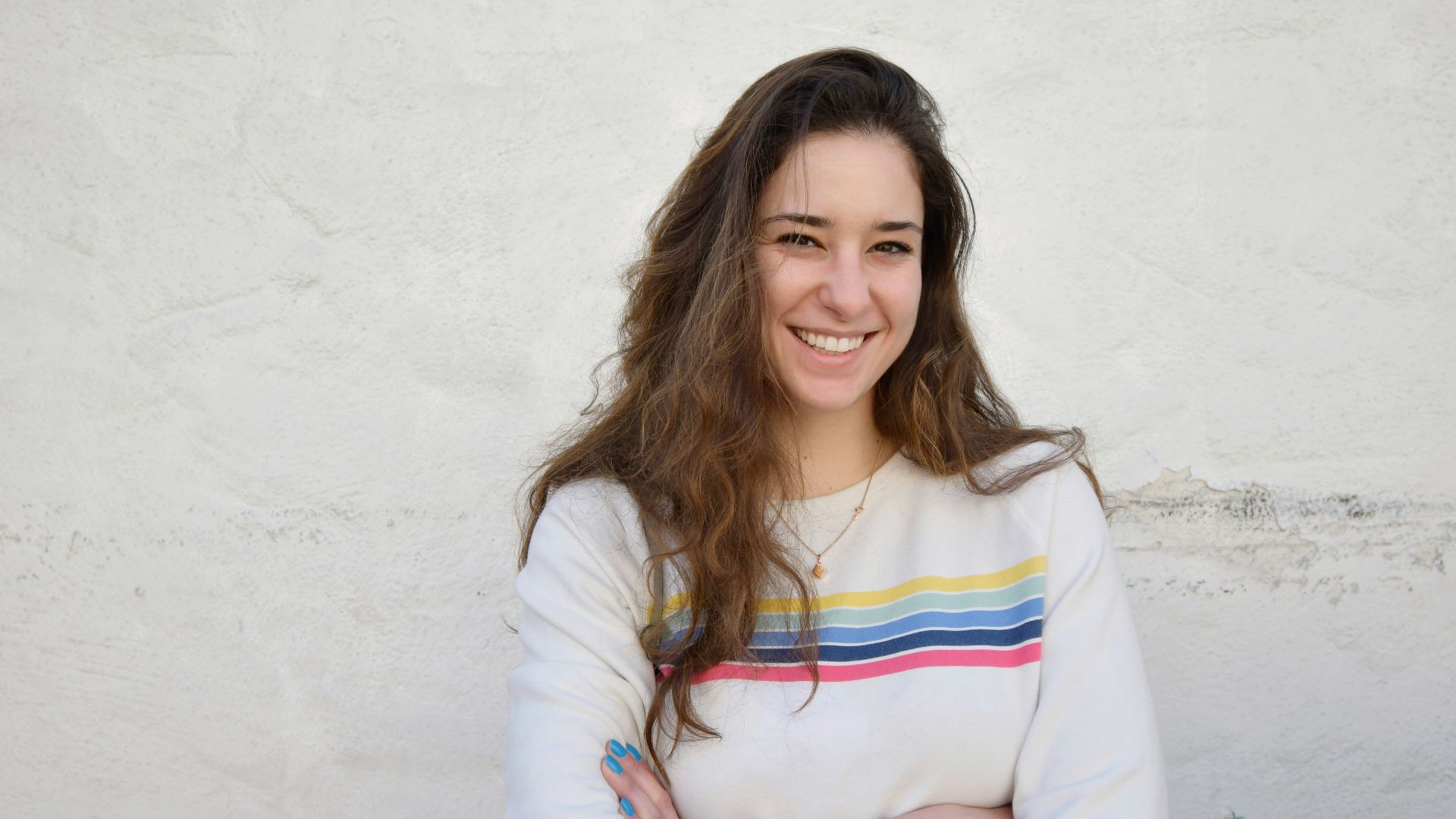 a woman standing with her arms crossed in front of a white wall
