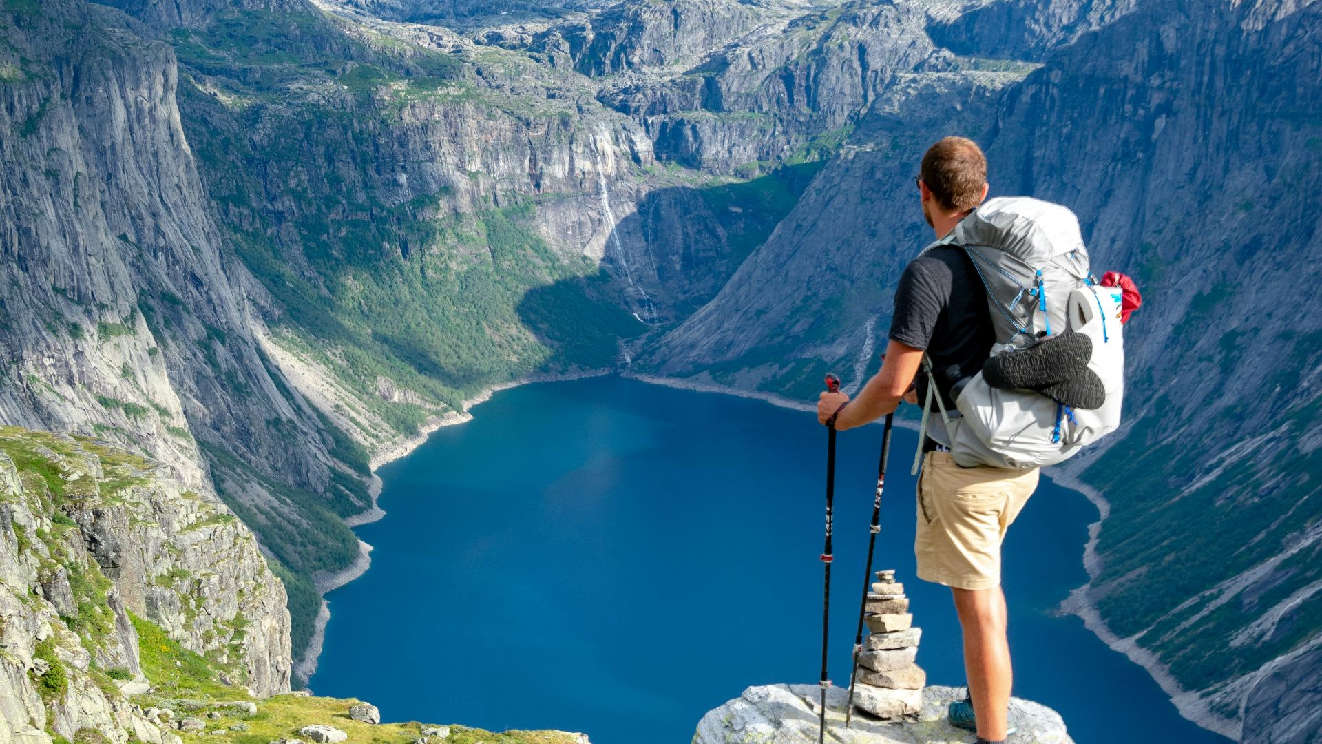 man standing on rock looking towards lake