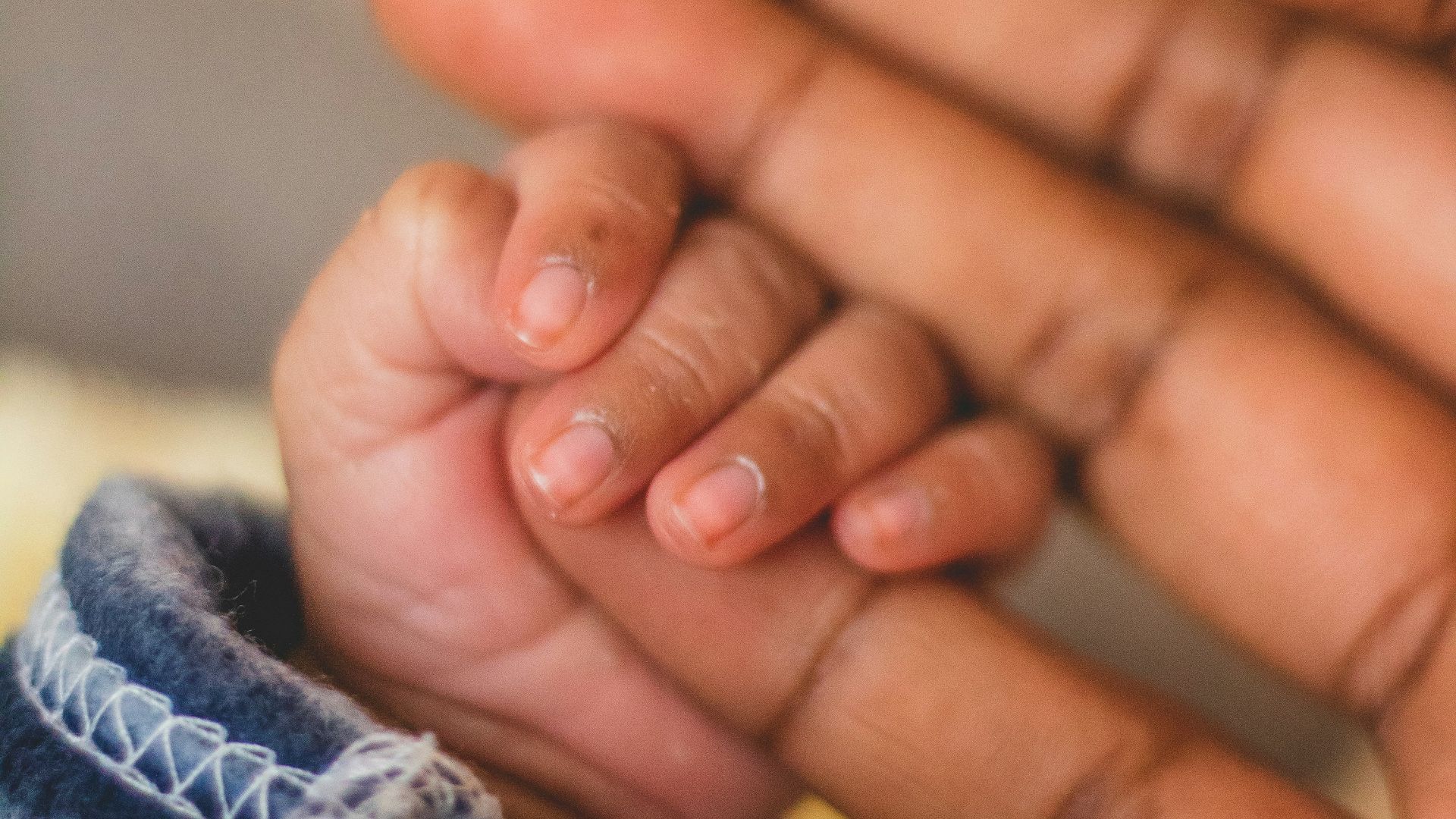 child's hand gripping person's pinkie finger