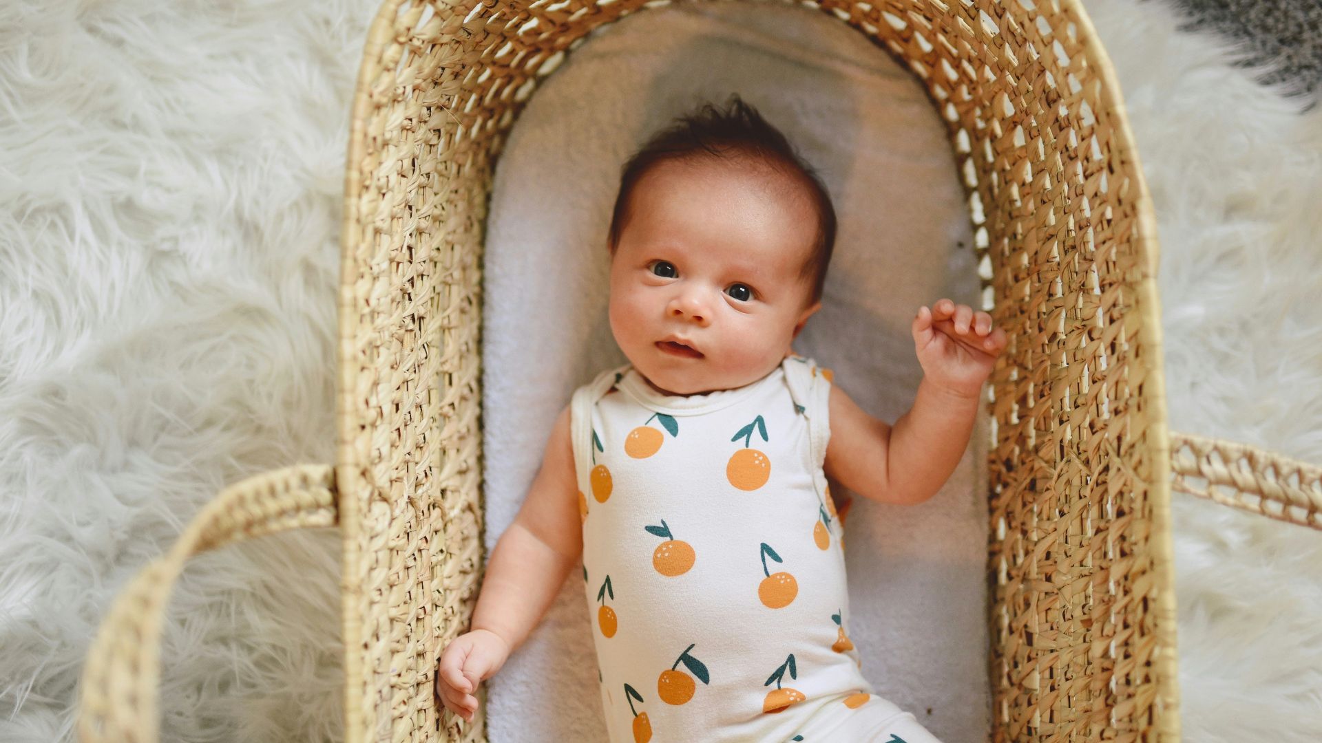baby in white and green polka dot onesie lying on brown wicker basket