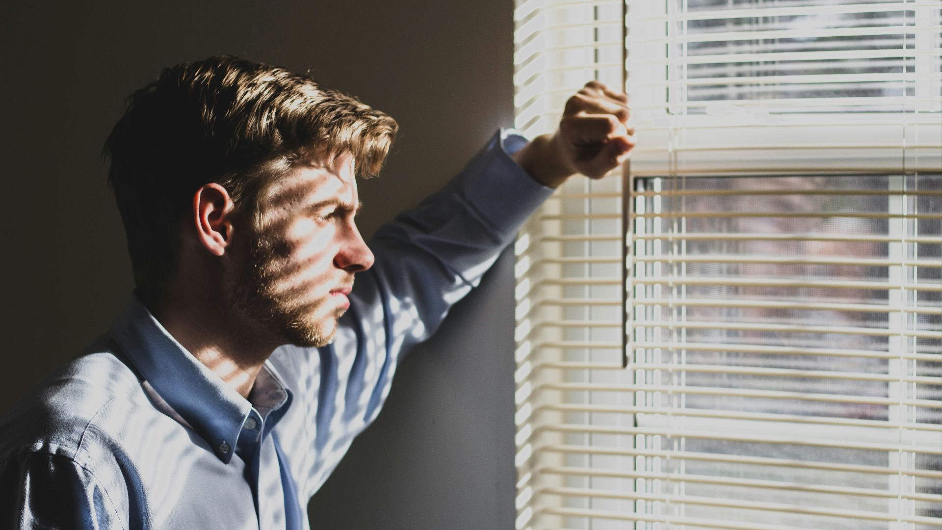 person near clear glass window pane and window blinds low-light photography