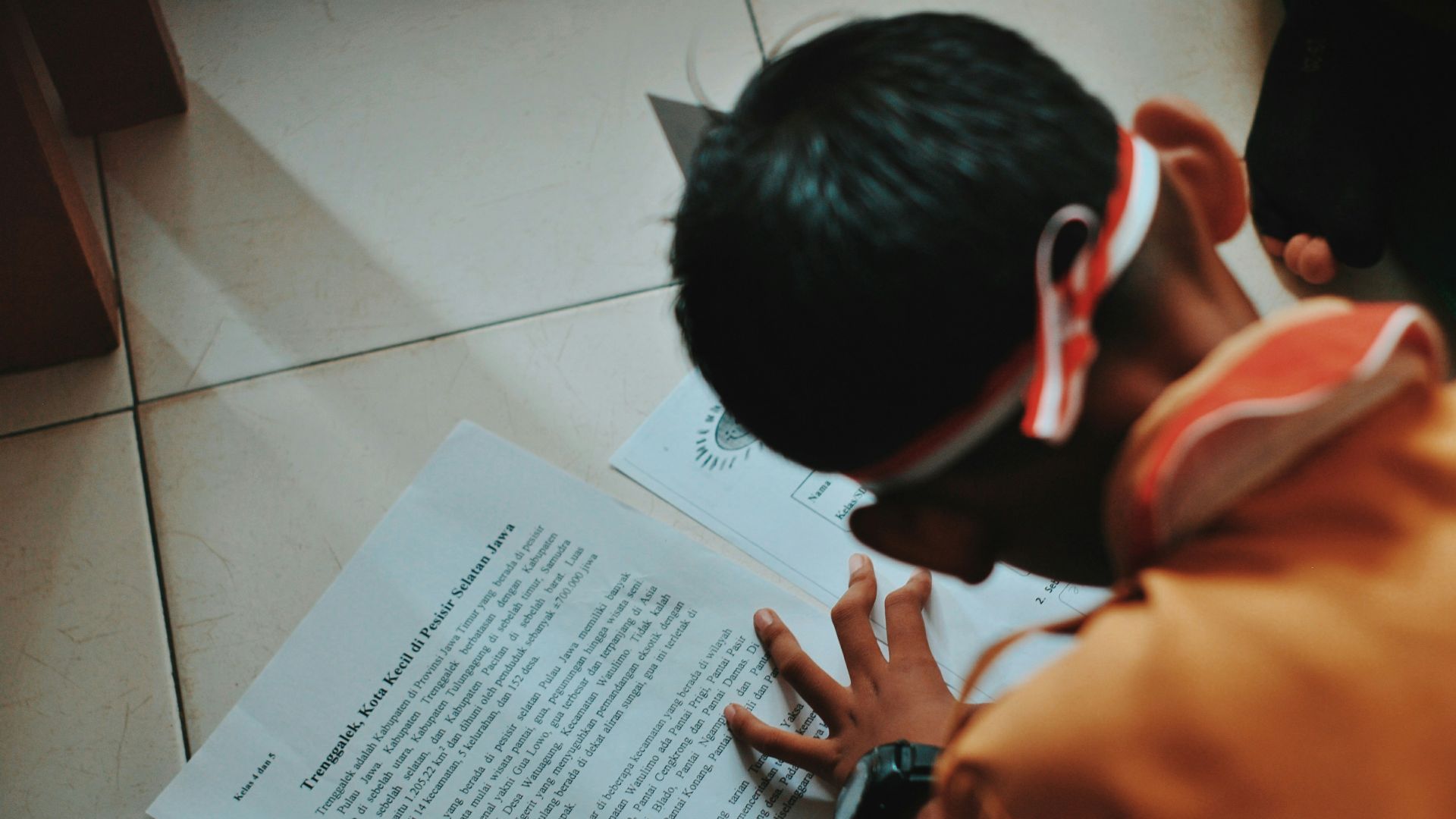 man in orange shirt writing on white paper