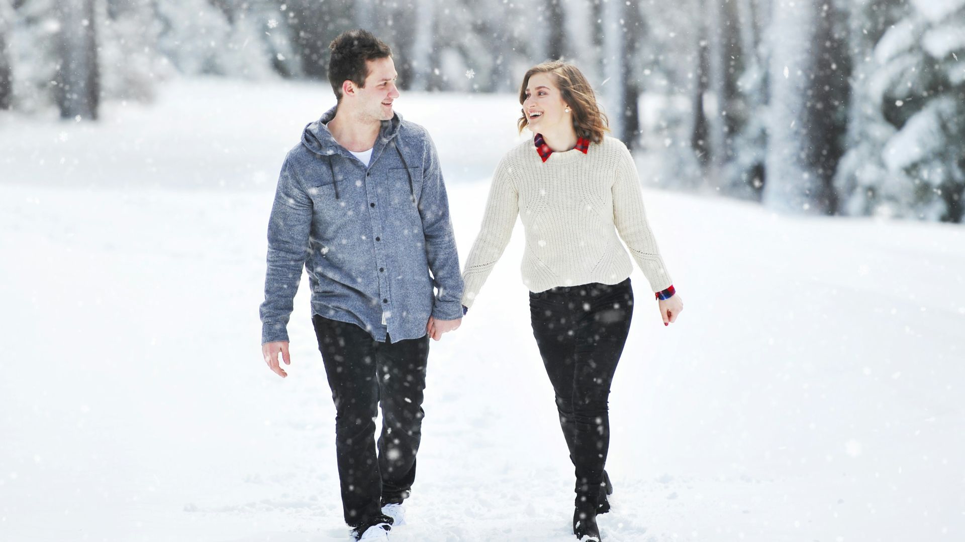 couple walking on snow near trees during daytime