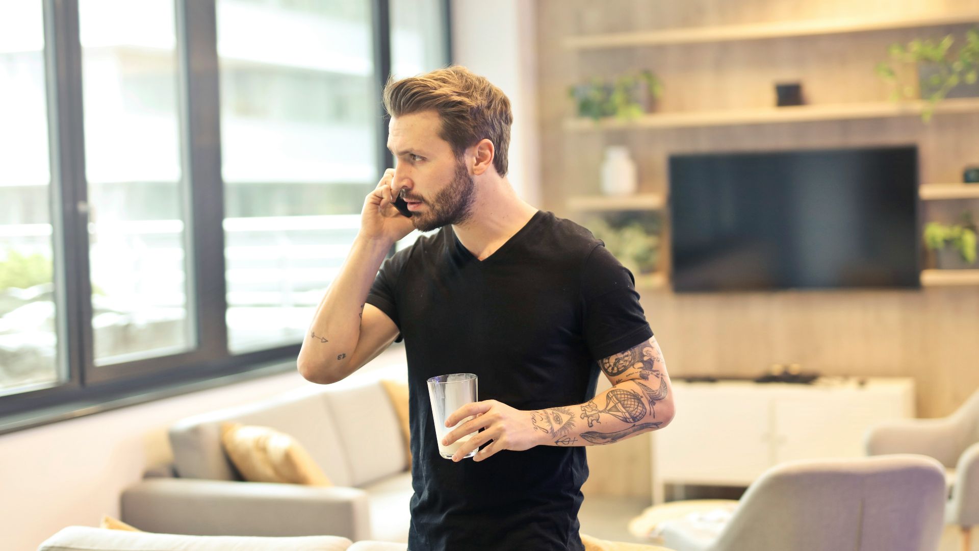 man holding drinking glass while taking a call on phone