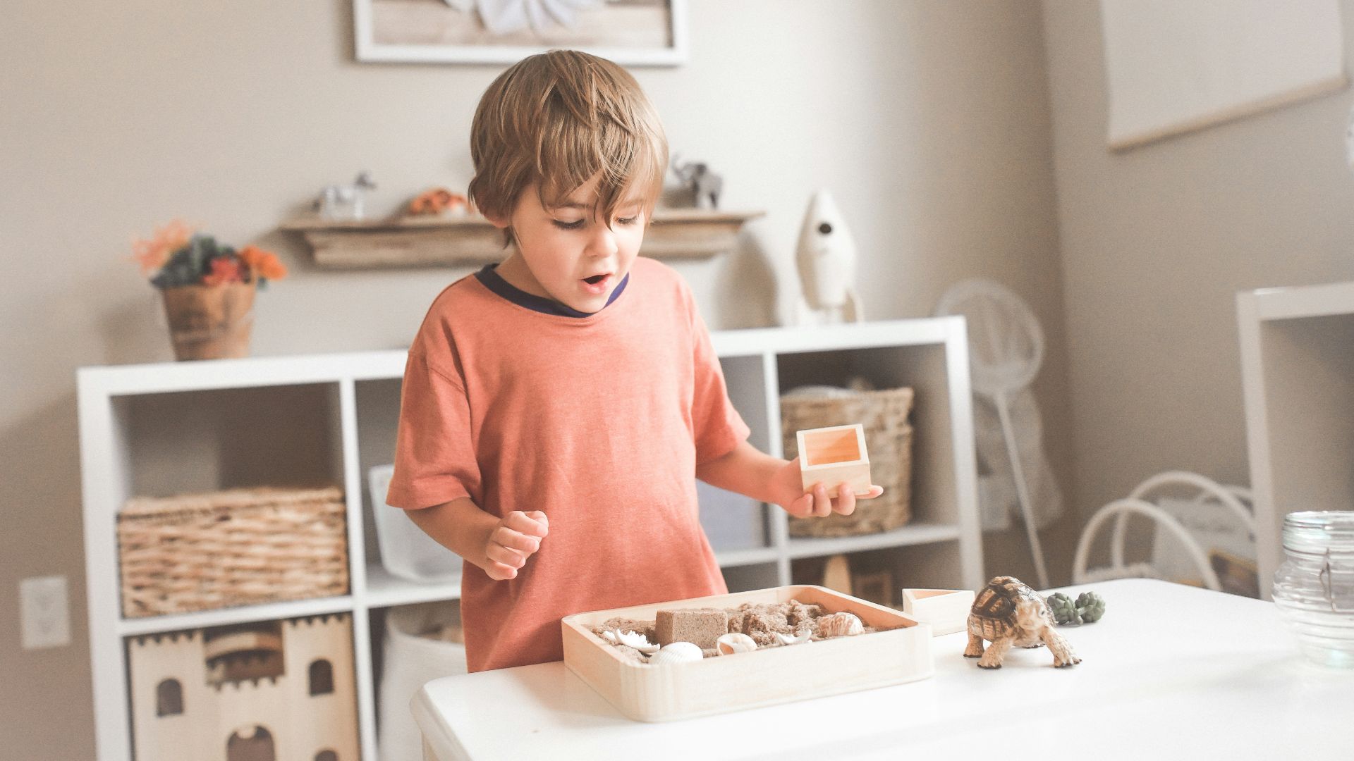 boy in orange crew neck t-shirt standing in front of white wooden table with cupcakes