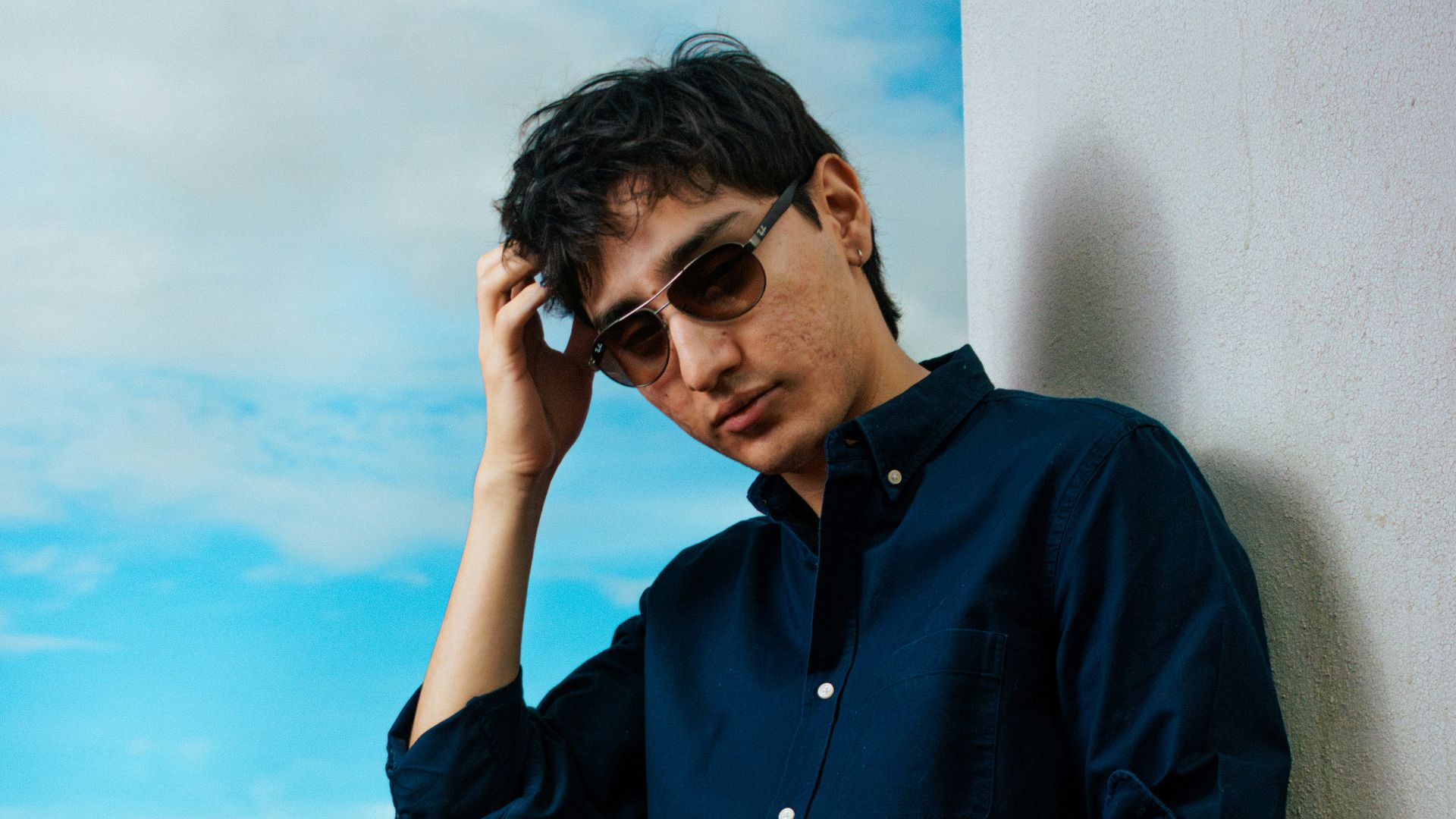 Man in sunglasses crouches against a wall