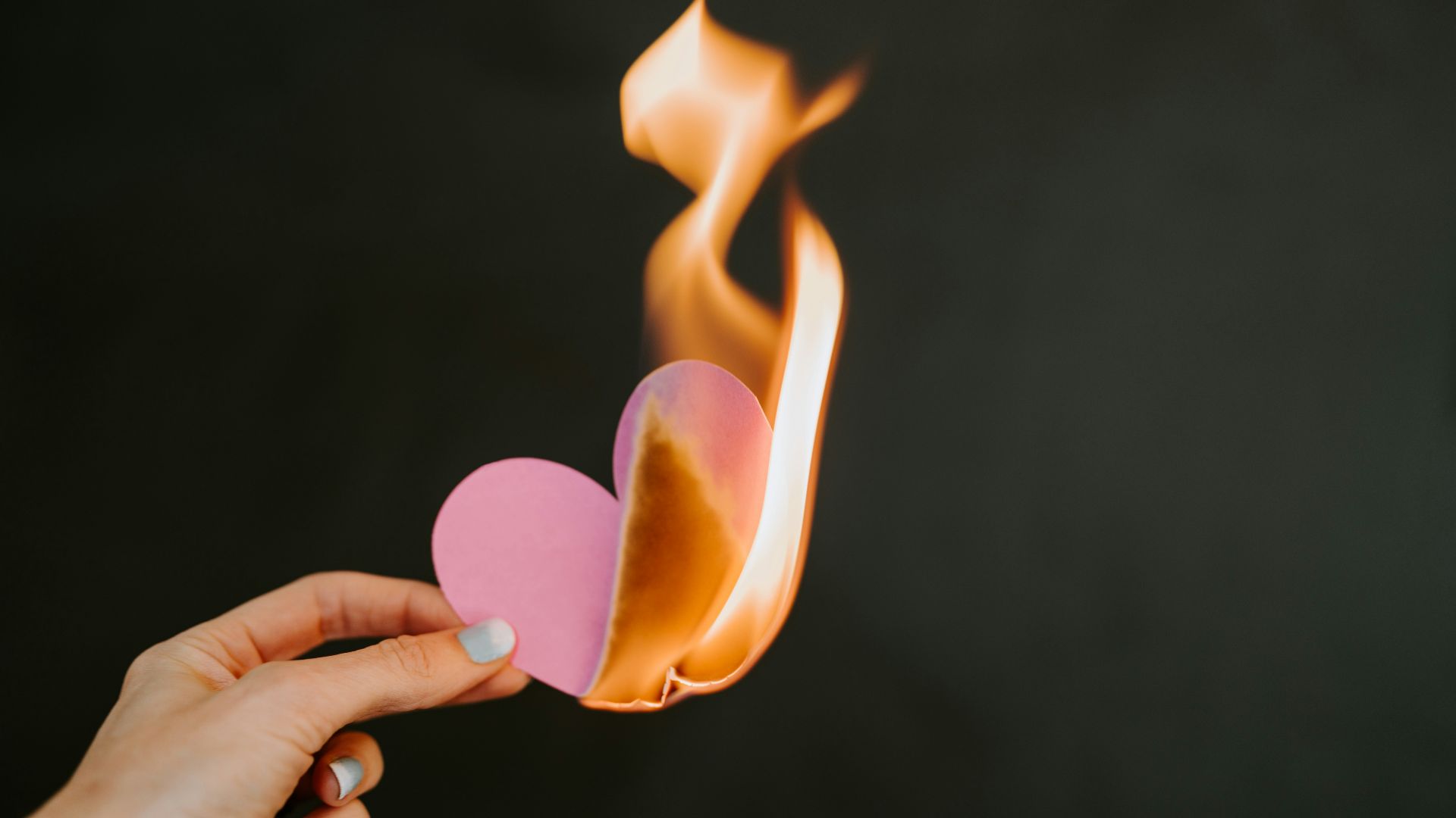 a person holding a paper heart in front of a fire