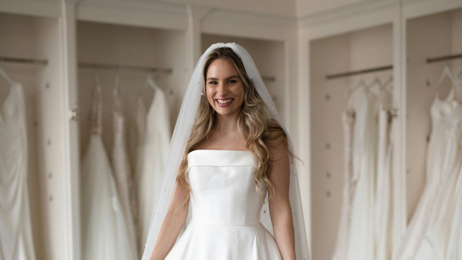 a woman in a wedding dress standing in front of a rack of dresses
