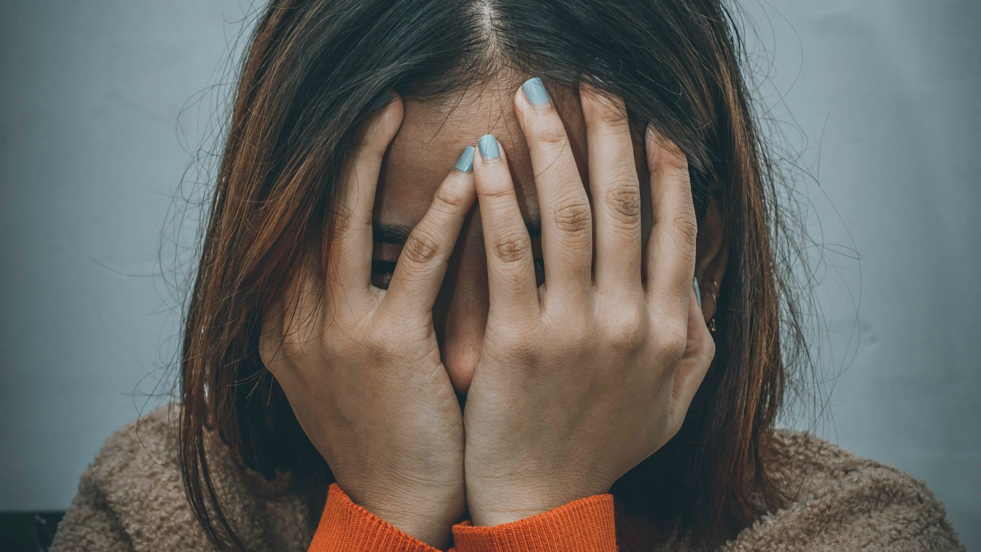 woman in brown sweater covering her face with her hand