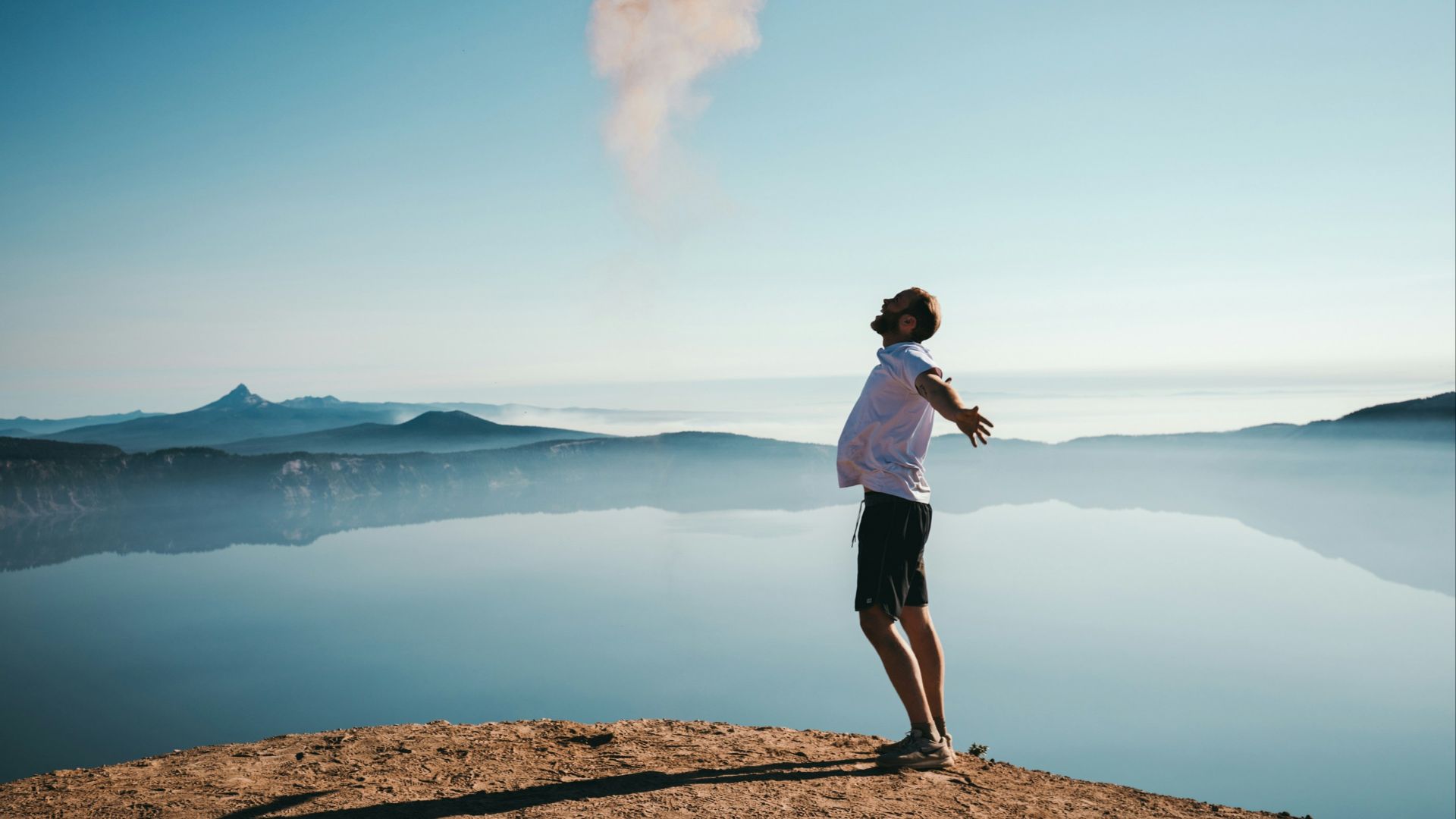 man standing on sand while spreading arms beside calm body of water