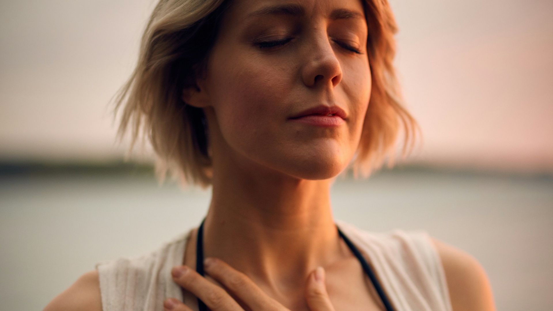 woman in white vest and black bikini with hand on chest