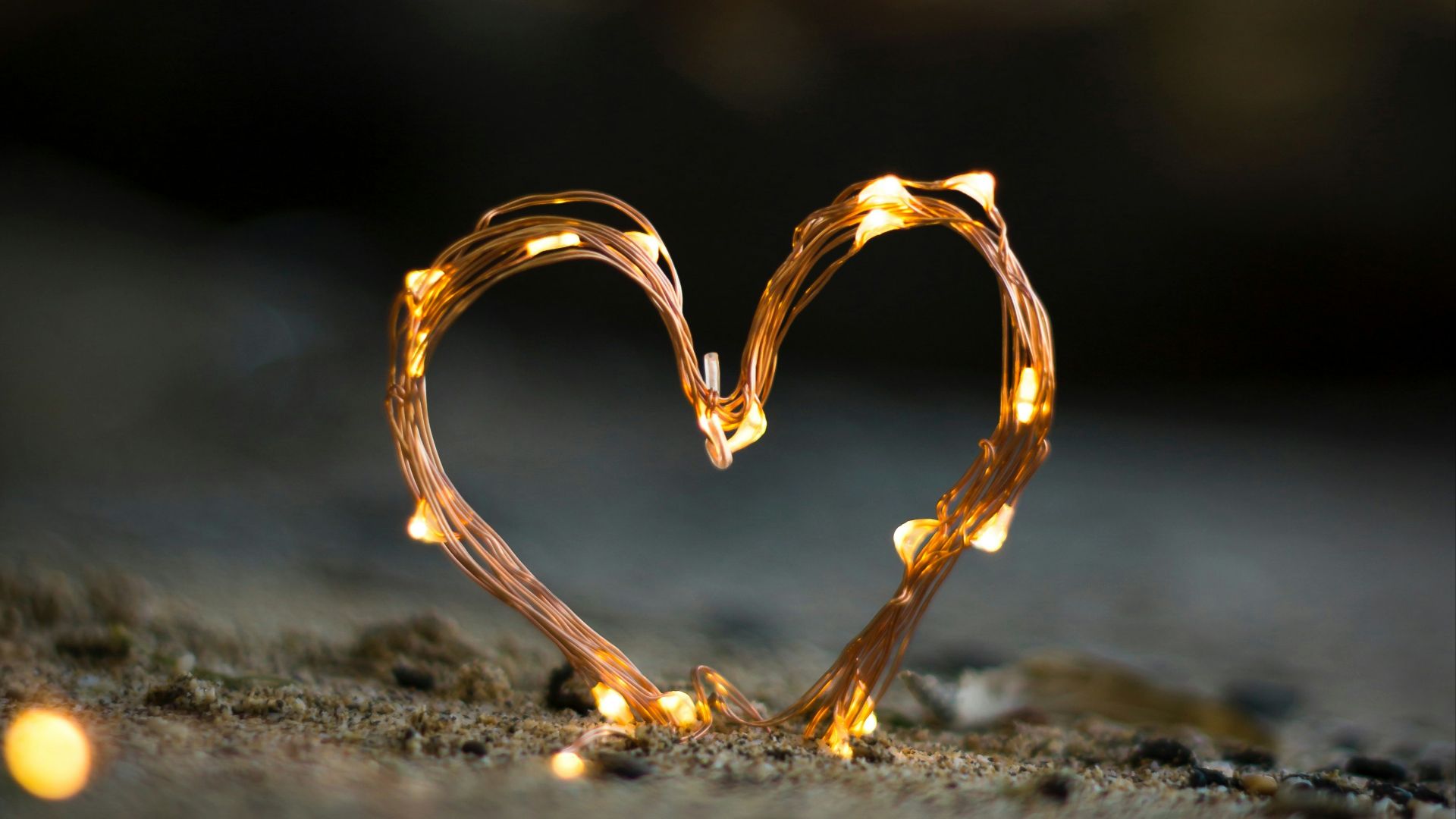 close-up photography of heart shaped fairy lite on brown sand