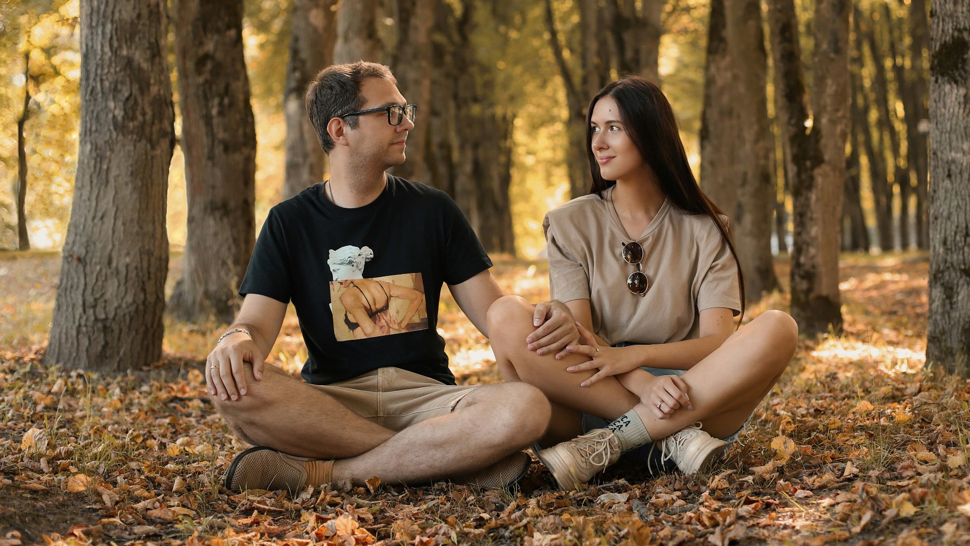 a man and a woman sitting on the ground in a forest