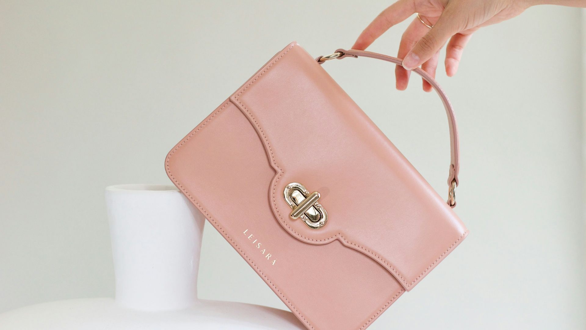 a woman holding a pink purse over a white vase