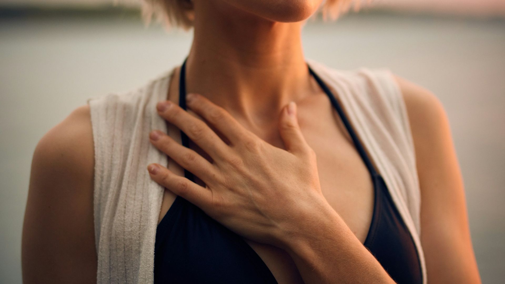 woman in white vest and black bikini with hand on chest