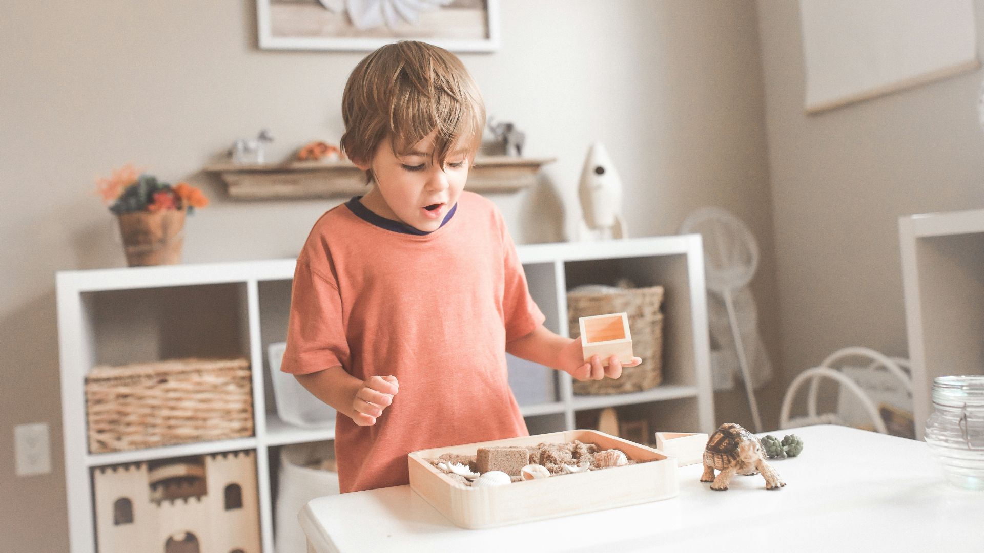 boy in orange crew neck t-shirt standing in front of white wooden table with cupcakes