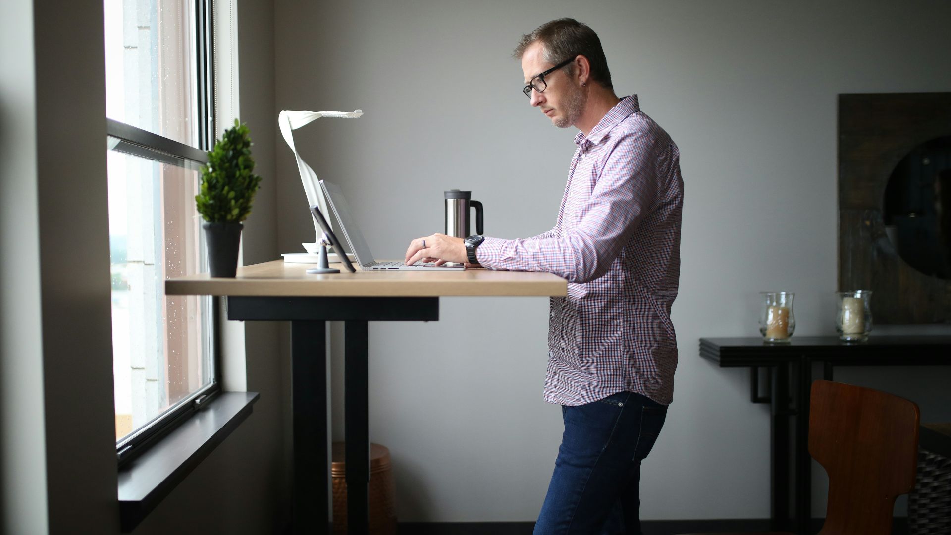 man in pink dress shirt and blue denim jeans standing beside brown wooden table