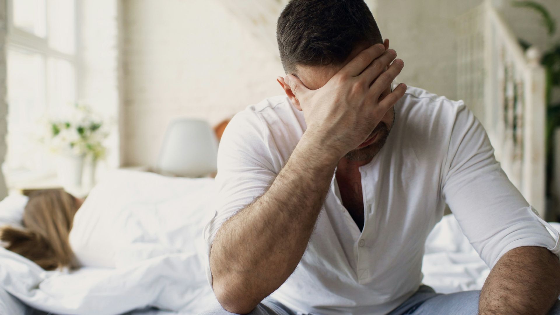 Man sitting on bed with hand over face