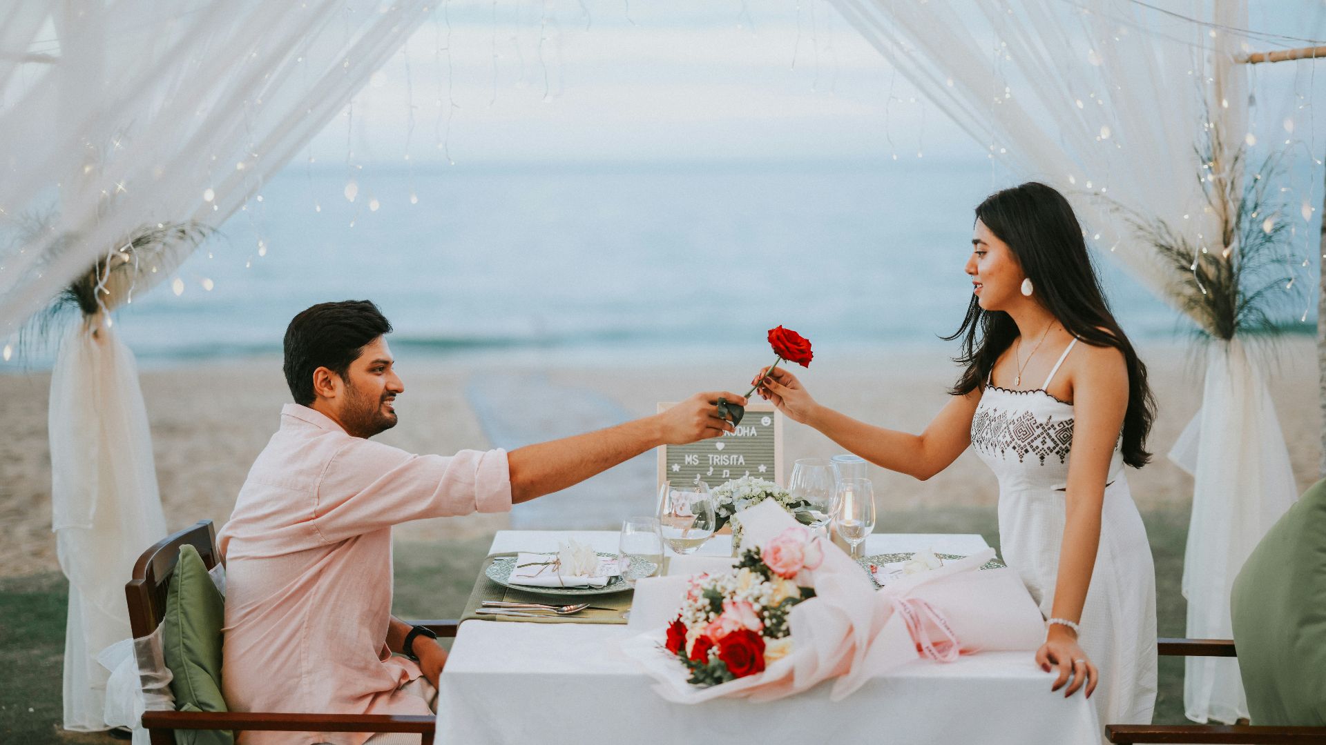 Man gives woman a rose at a beach dinner.