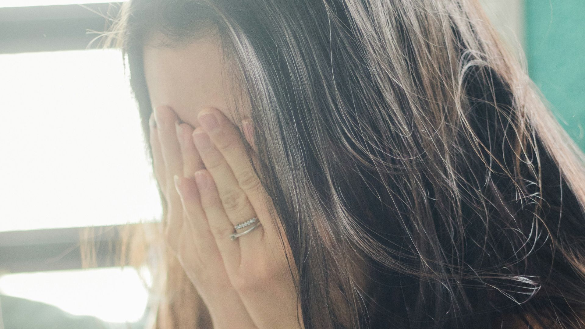 woman in brown shirt covering her face