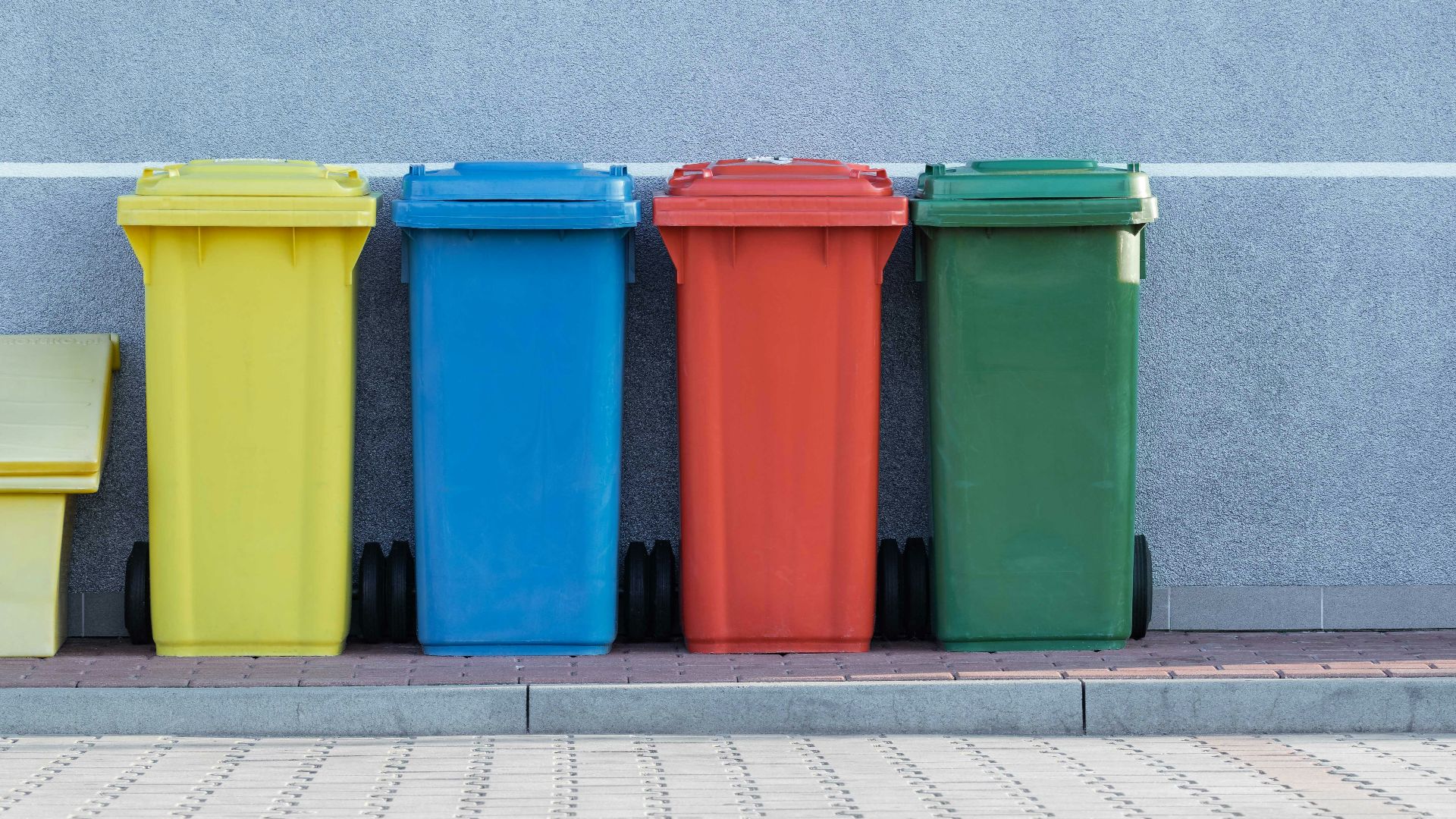 four assorted-color trash bins beside gray wall