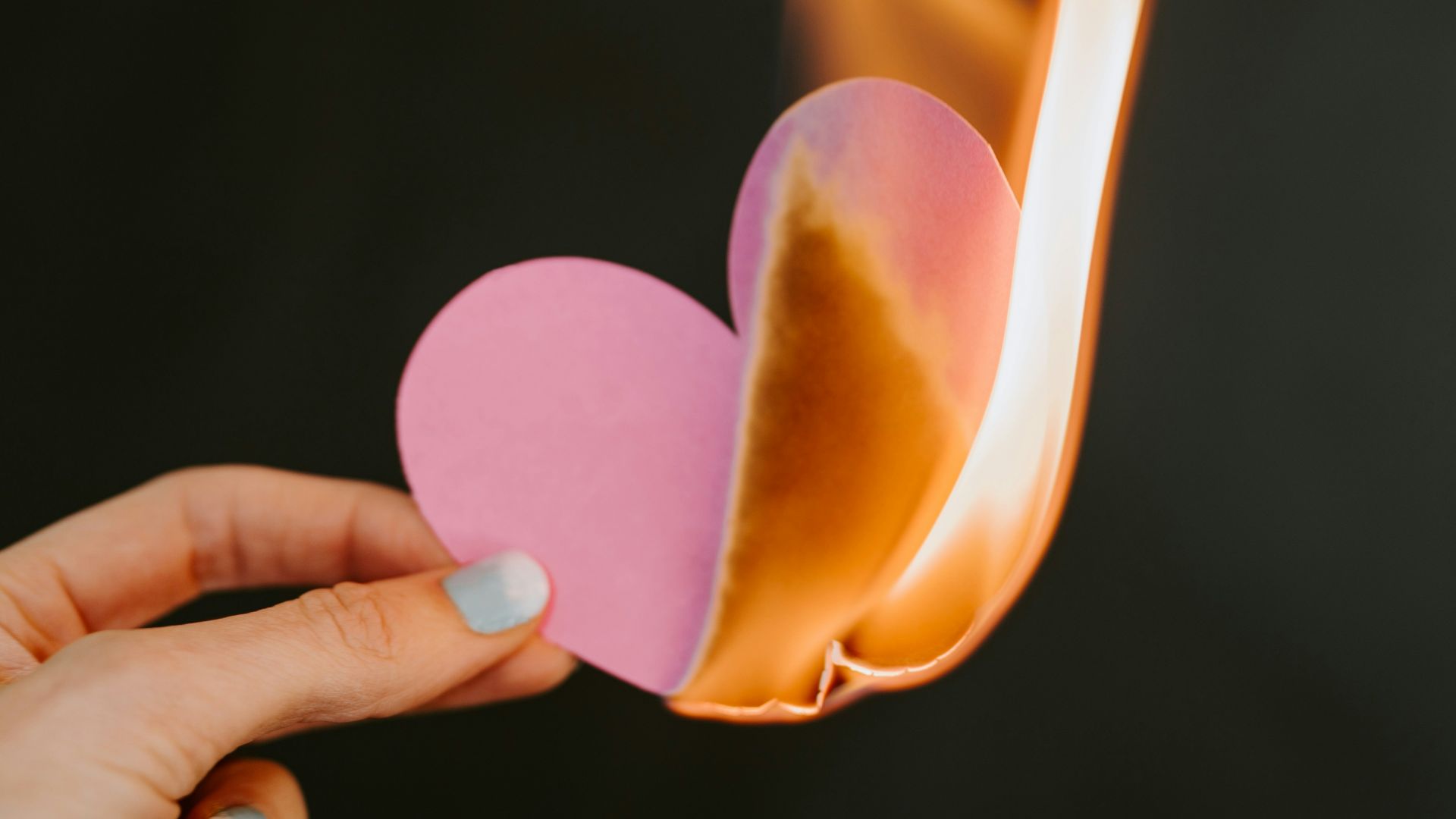 a person holding a paper heart in front of a fire