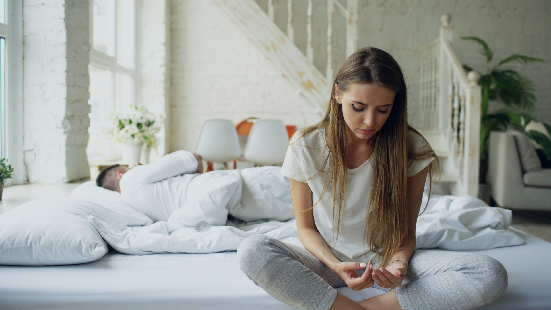 Woman sitting on bed, man sleeping behind her
