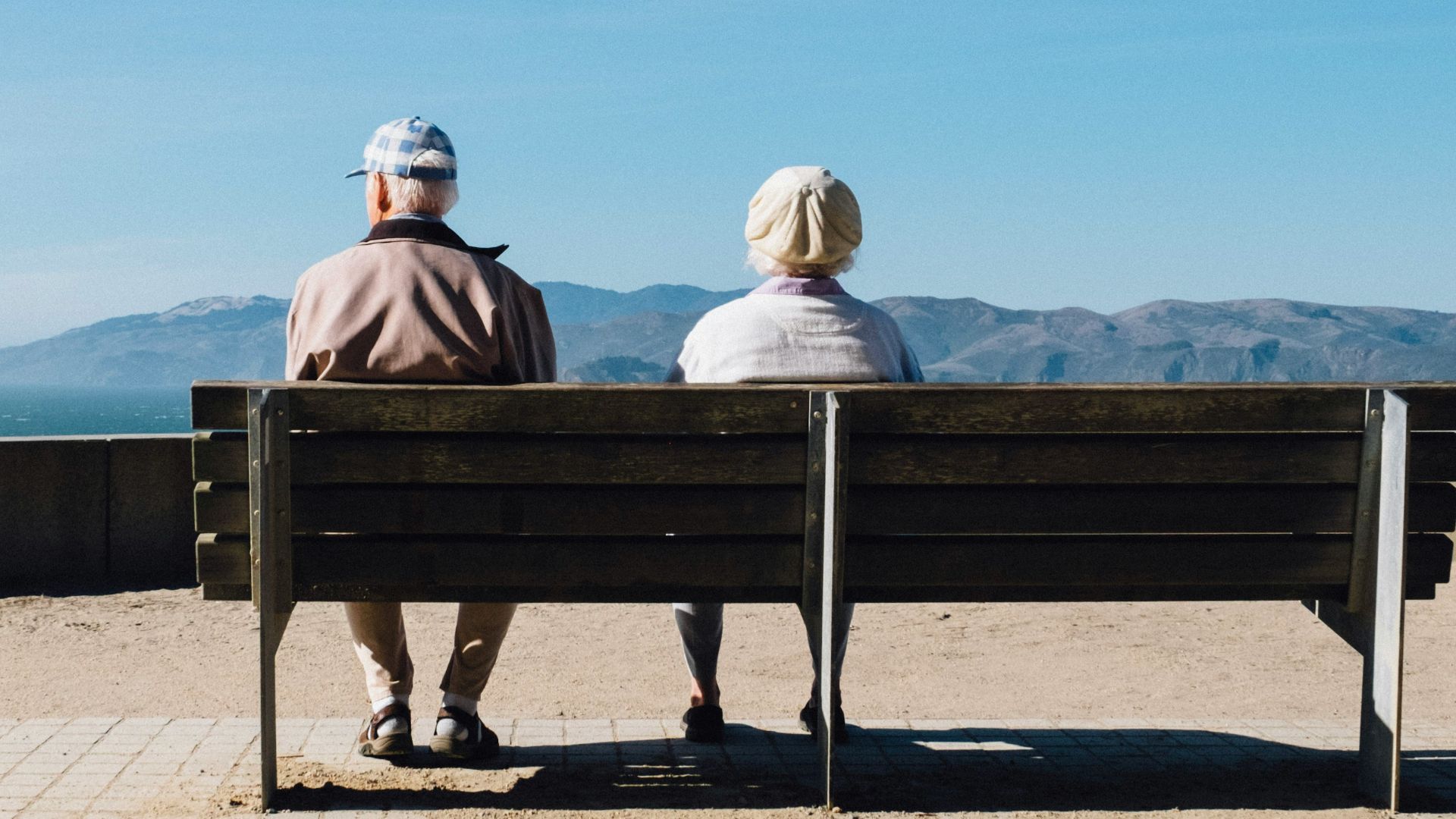 man and woman sitting on bench facing sea