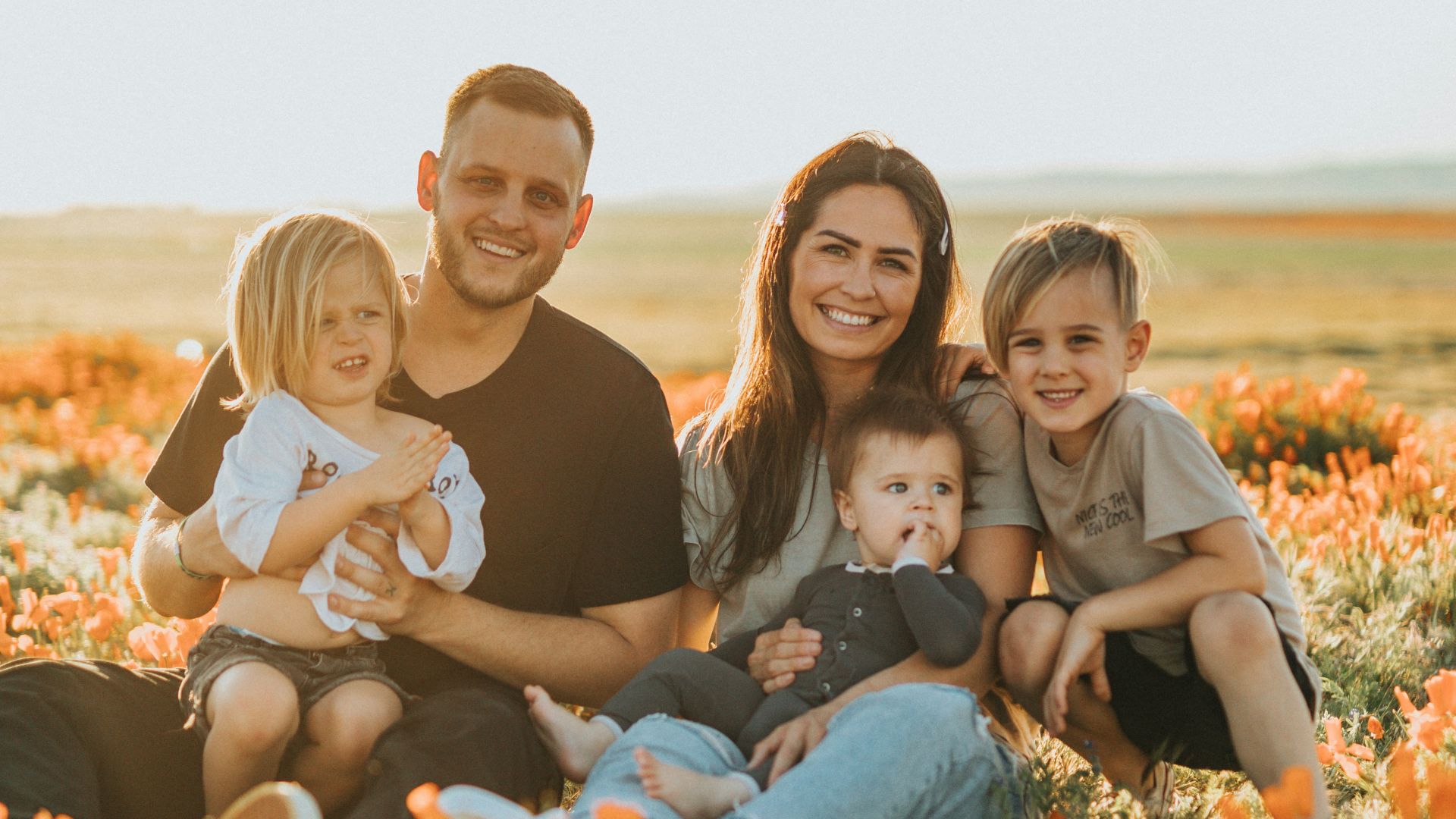 3 women and 2 men sitting on green grass field during daytime