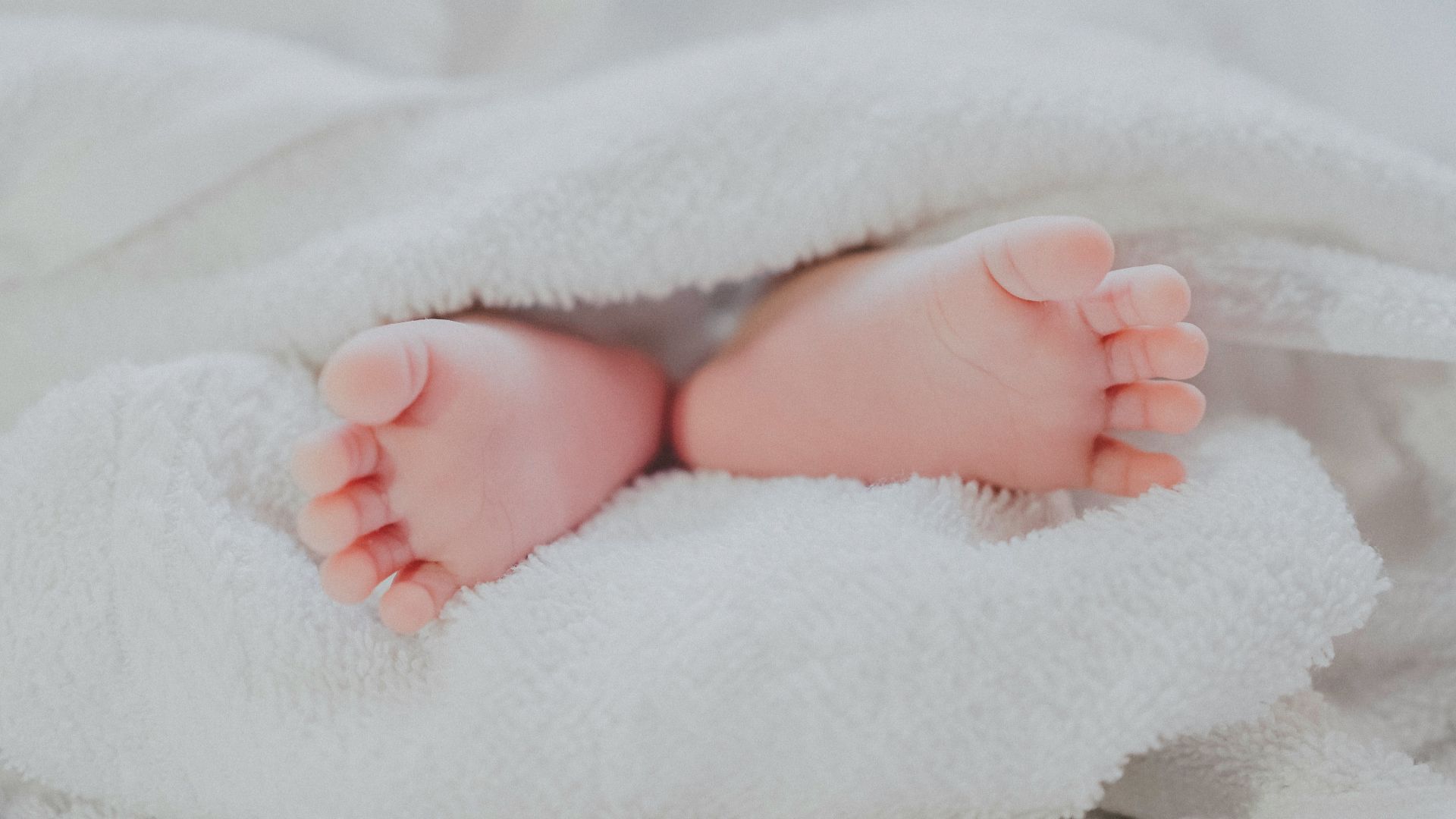 barefooted baby covering white blanket