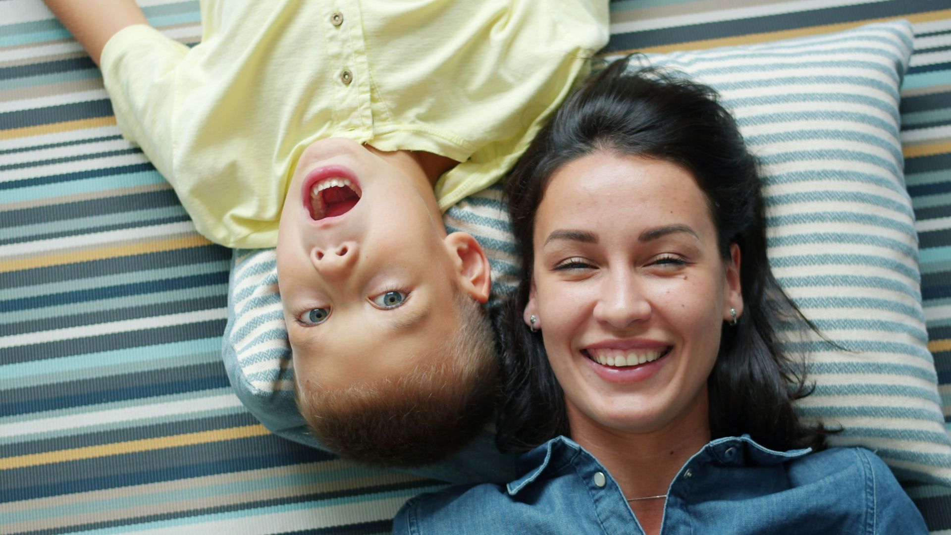 Mother and son lying on striped rug smiling