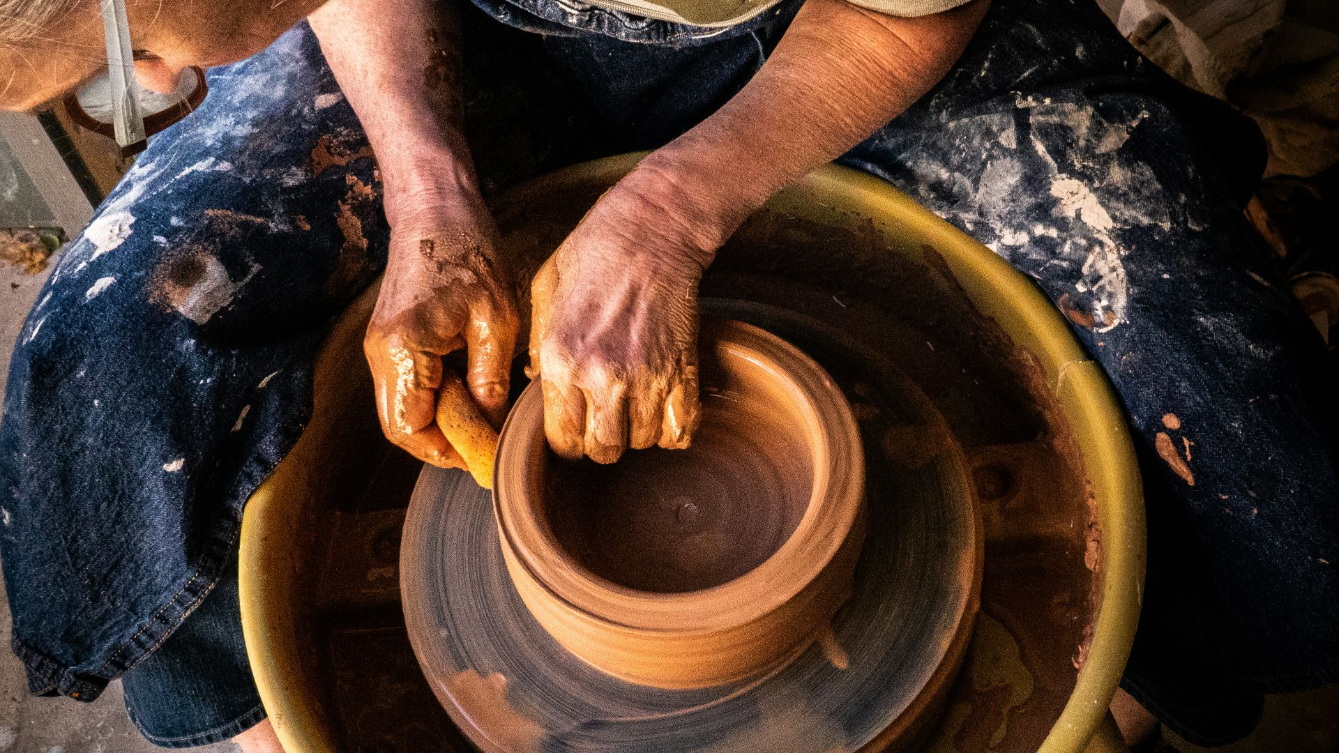 person in blue denim jeans making clay pot