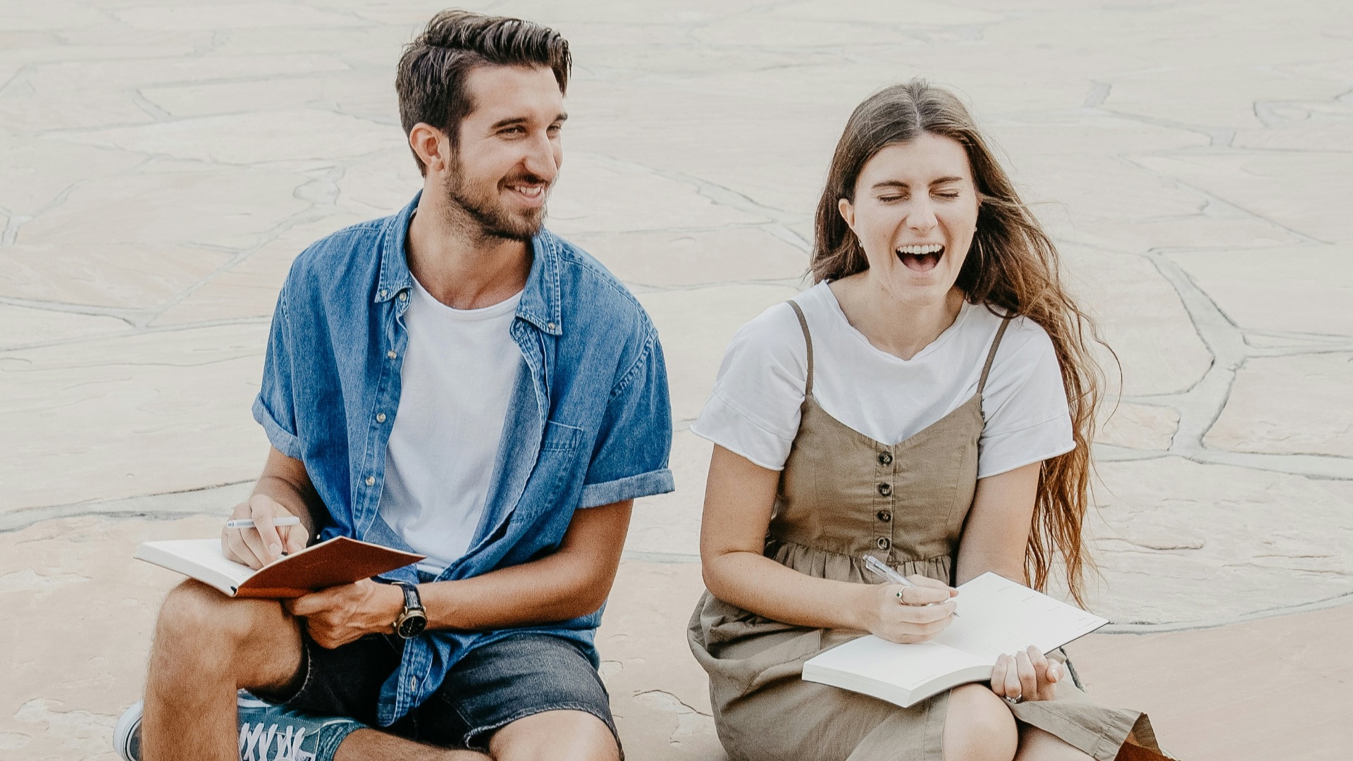 man and woman sitting side by side holding notebooks