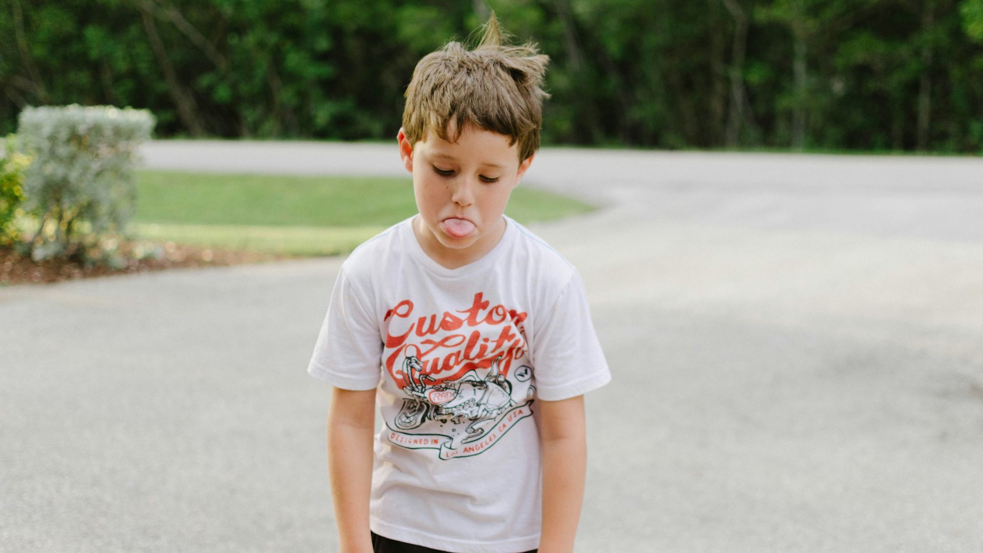 boy standing on gray concrete road while tongue out
