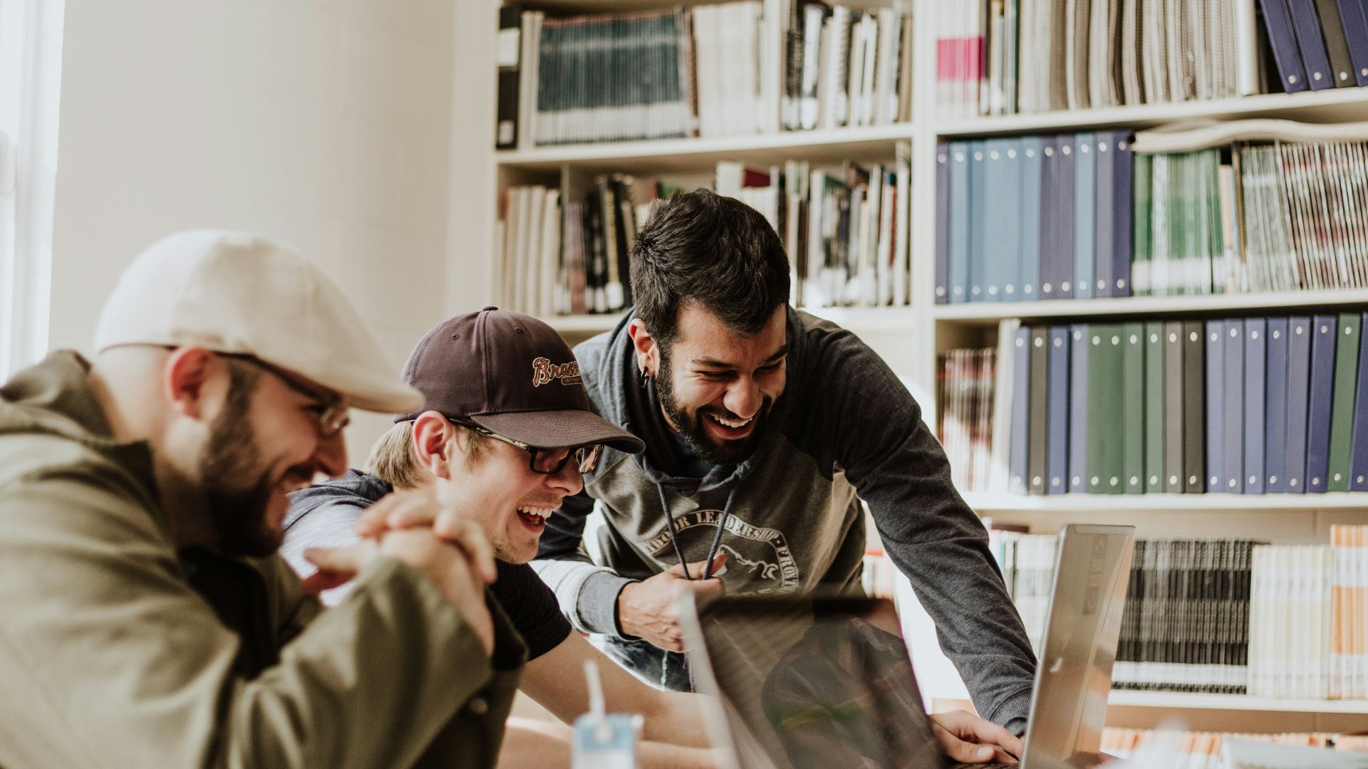 three men laughing while looking in the laptop inside room
