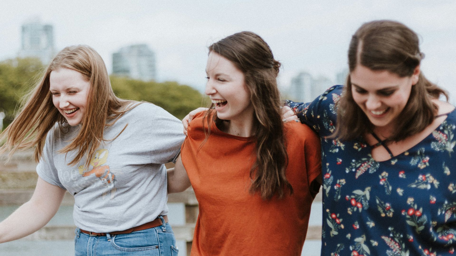 three women walking on brown wooden dock near high rise building during daytime
