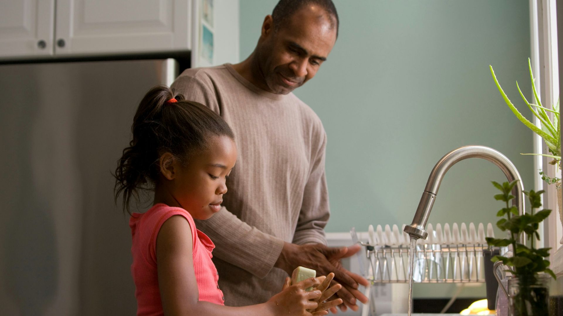 man in long sleeve shirt standing beside girl in pink tank top washing hands